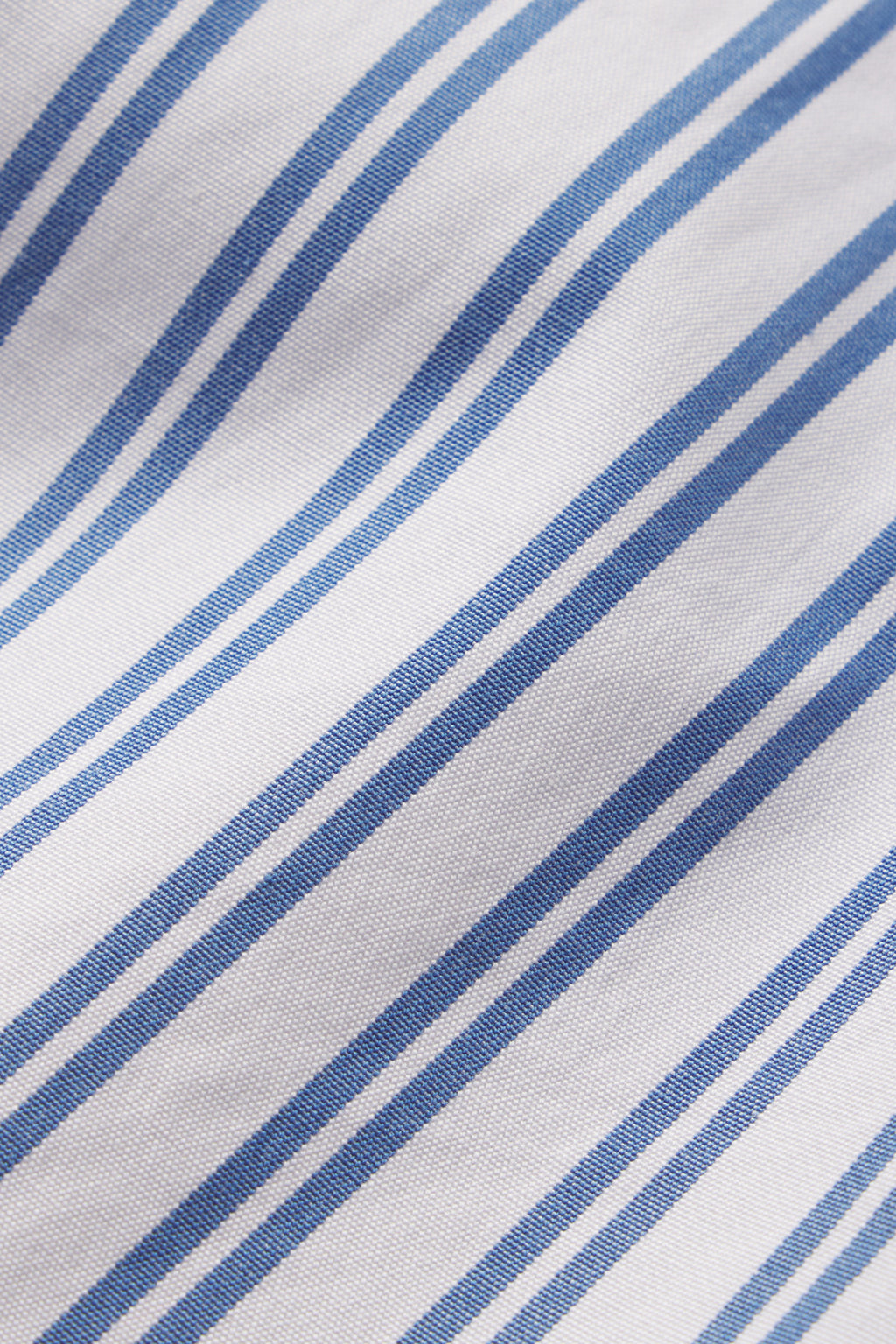 A close-up of the Poplin Chloe Pajama Set in Seaport Shoreline Stripe shows white cotton poplin with blue stripes of varying thickness, creating a simple, clean pattern with visible fabric texture.