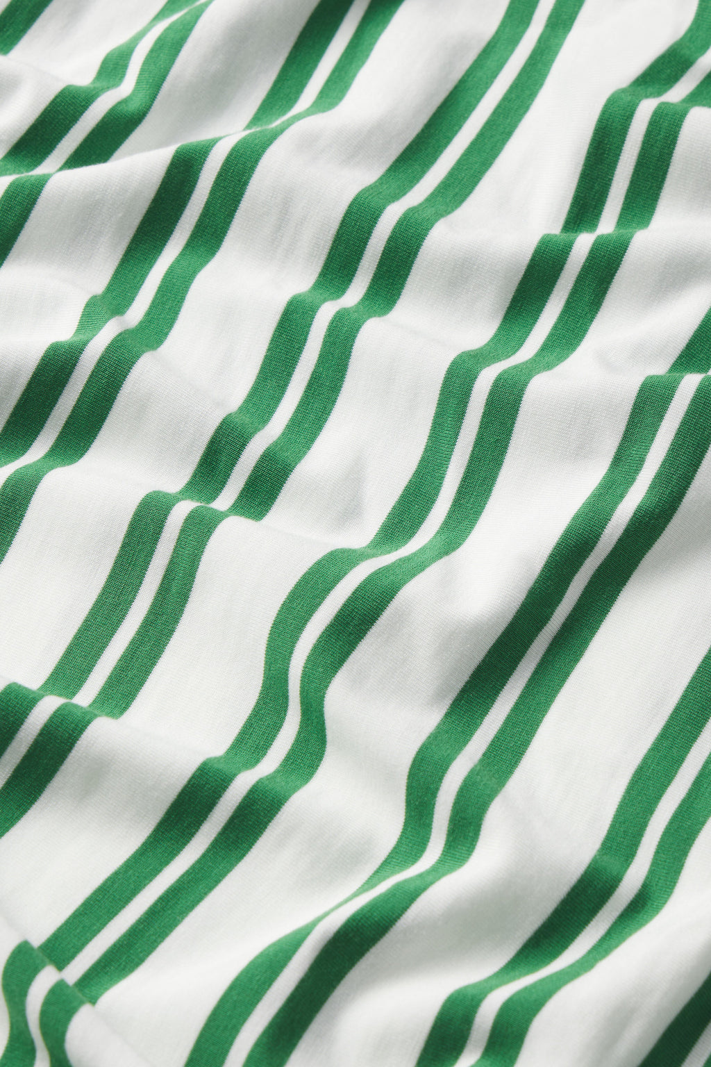 A close-up of the DreamModal Daydream Pants Set in Palm Stripe, showing white fabric with green wavy vertical stripes, abstract folds, and soft shadows.