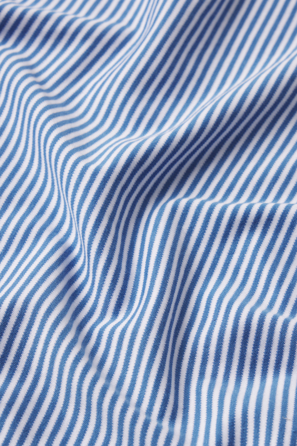 Close-up of Seaport Stripe pattern on the Pima Short Robe, featuring blue and white diagonal pinstripes on textured cotton, with gentle folds creating soft shadows and movement.
