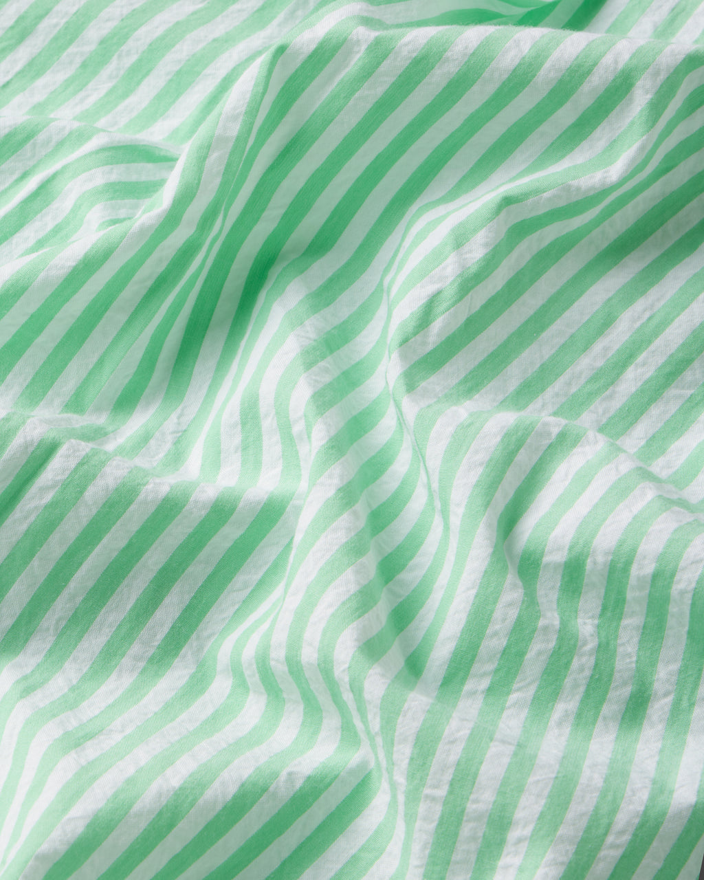 Green and white striped Clover Leaf Seersucker fabric drapes in gentle waves, with lighting accentuating the texture and movement of the Alice Nightgown.