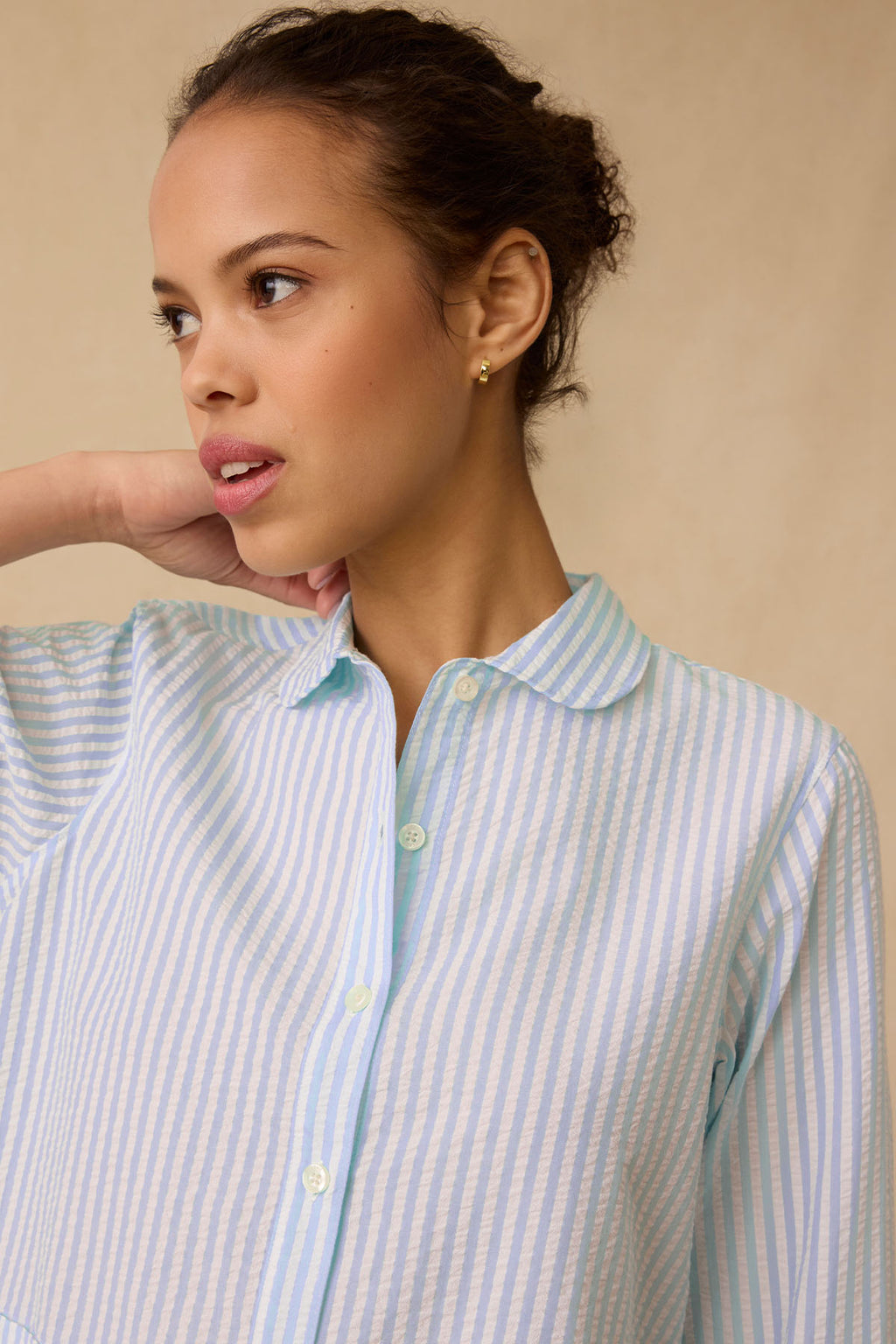 A woman wearing the Georgie Pocket Shorts Set in Salt Spray Seersucker looks to the side with a neutral expression against a beige background.