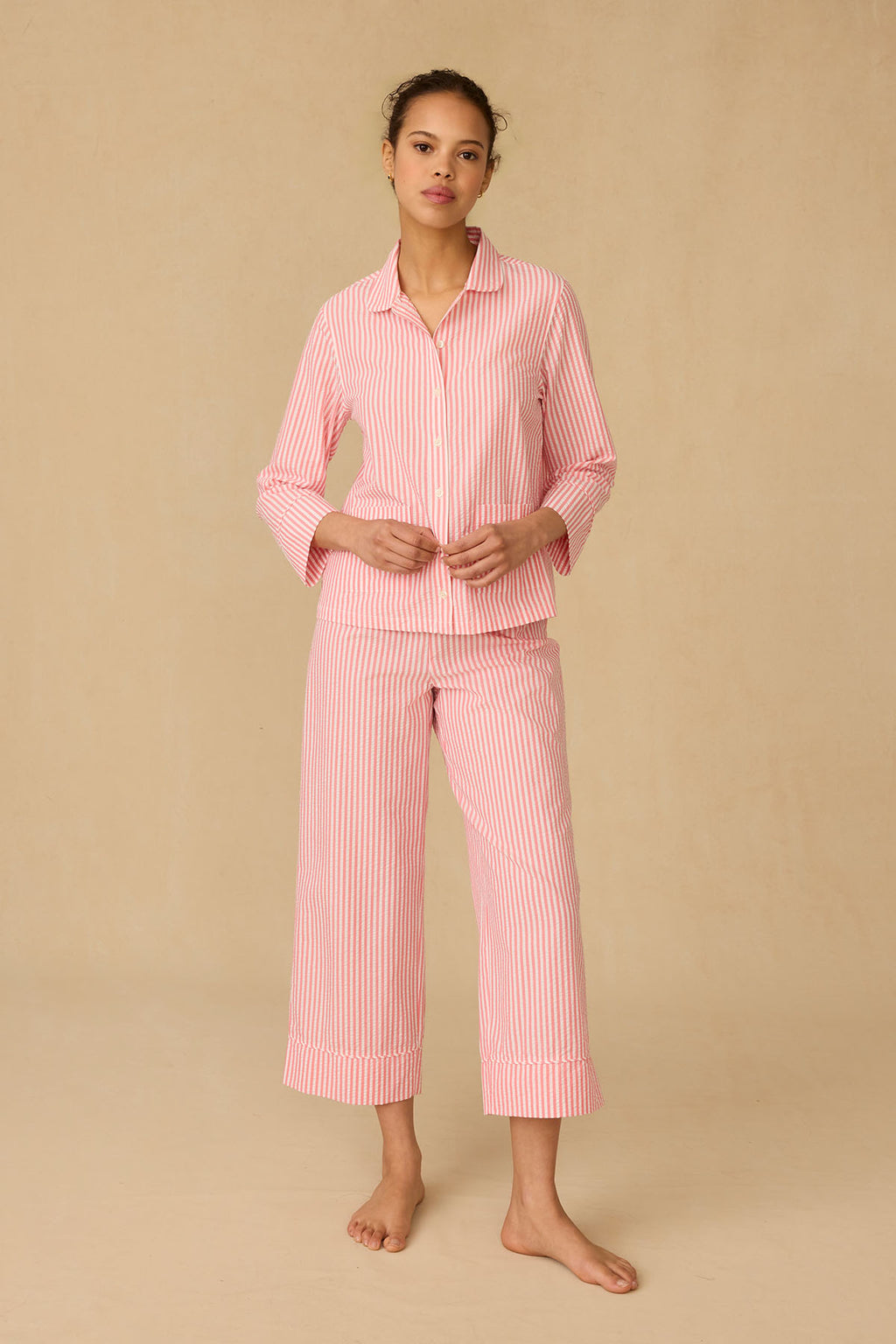 A person stands on a plain beige background, wearing the Georgie Pocket Pants Set in Gelato Seersucker, featuring a button-up long-sleeve top and wide-leg pants for ultimate comfort.