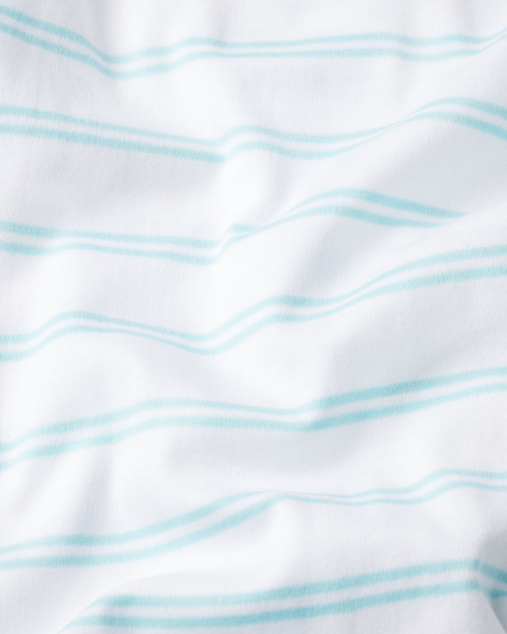 The Baby Sleeper in Beach Club Tidal Stripe is crafted from 100% Pima cotton, featuring white fabric with soft, light blue horizontal stripes and gentle turquoise double stripes for a charming, textured look.