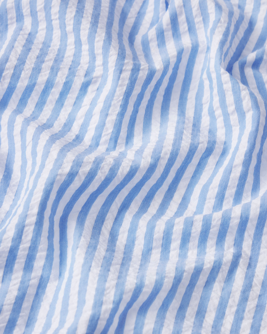 Close-up of the Georgie Pocket Shorts Set in Blue Seersucker, showing its blue and white stripes with textured creases and folds highlighted by light and shadow.