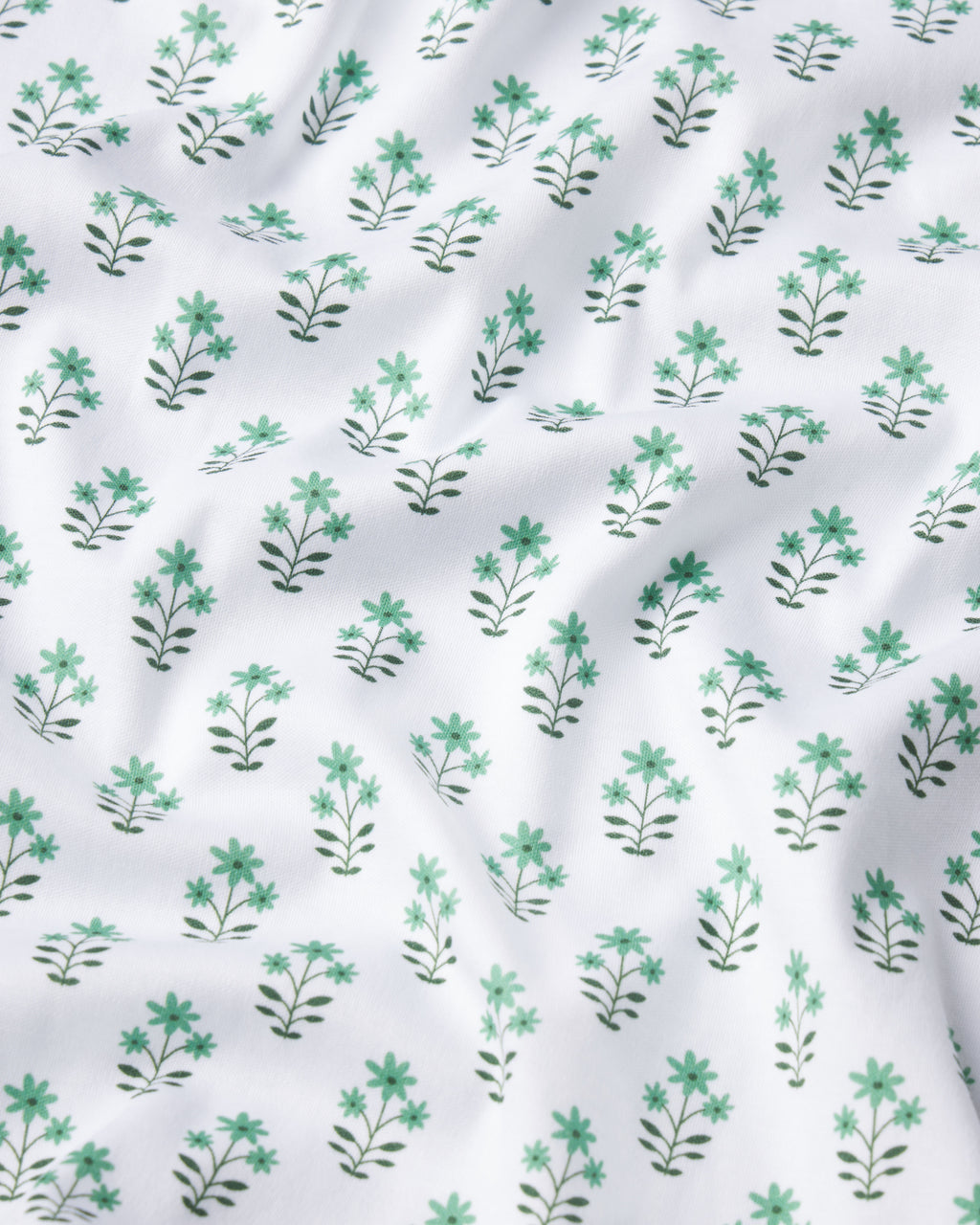 The Pima Long-Short Set in Boxwood Posy features soft Pima Cotton with a white base, adorned by a repeating pattern of green leafy plants and blue-green flowers. Its gentle texture creates subtle waves and a fresh, airy appearance.