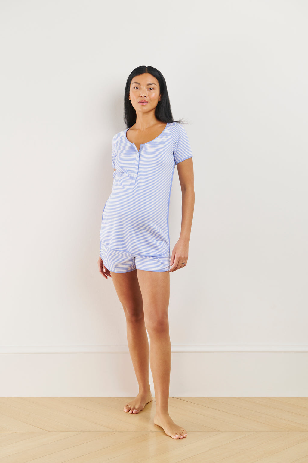 A pregnant woman stands barefoot against a light-colored wall, wearing the Pima Maternity Shorts Set in Hydrangea.