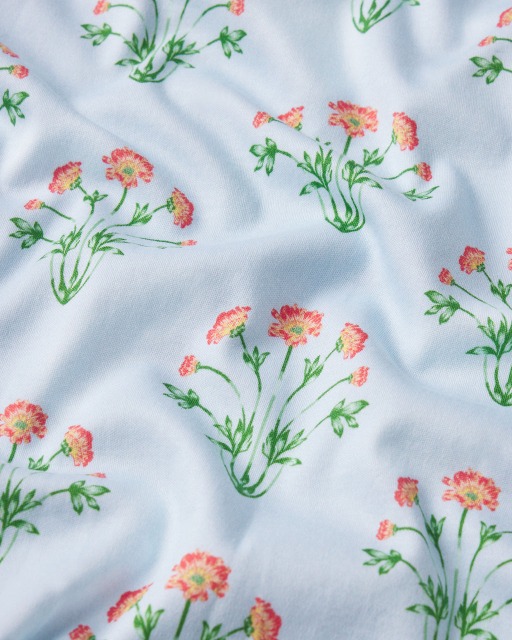 The Pima Ruffle Nightgown in Daylight Tropical Bouquet features light blue Pima cotton with small, hand-drawn pink and yellow flowers and green leaves—offering a gentle charm ideal for floral sleepwear.