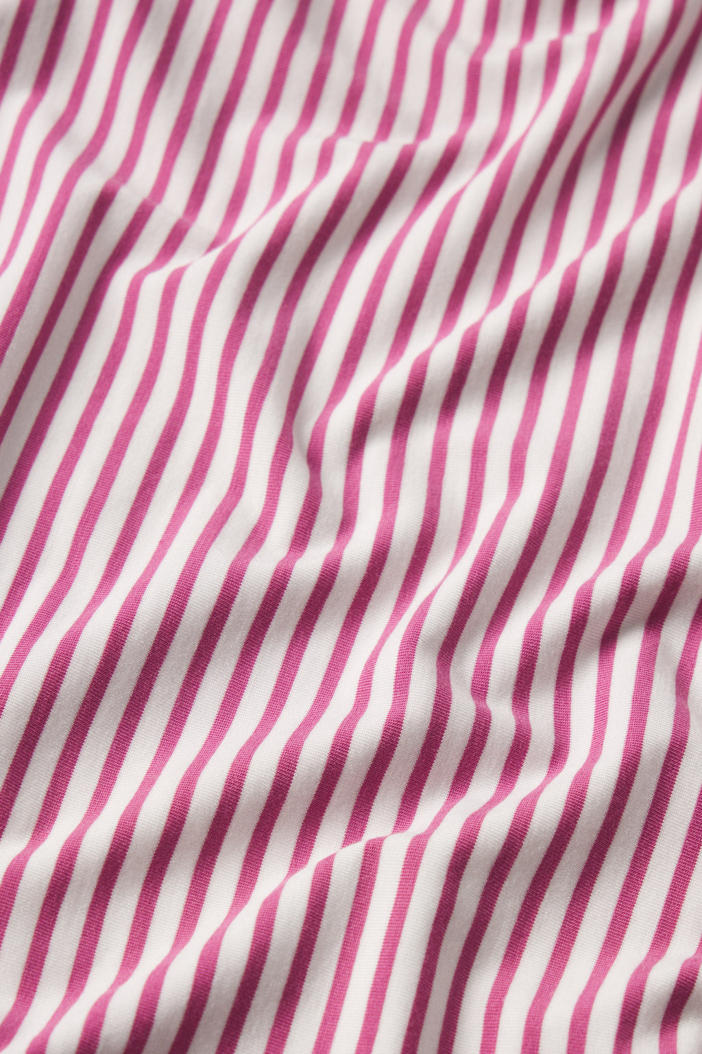 A close-up of the DreamModal Kimono Robe in Camellia Pencil Stripe shows soft, pink and white diagonal stripes on gently wrinkled fabric, creating elegant waves—perfect for a comfortable robe.