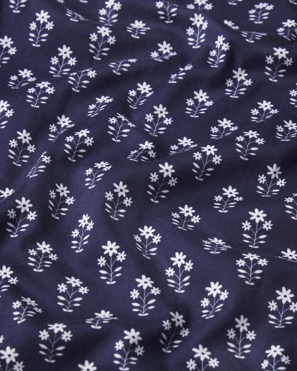 A close-up of the Pima Short-Long Set in English Navy Posy shows dark blue Pima cotton with a small white floral pattern and gentle folds—part of this cozy pajama set.