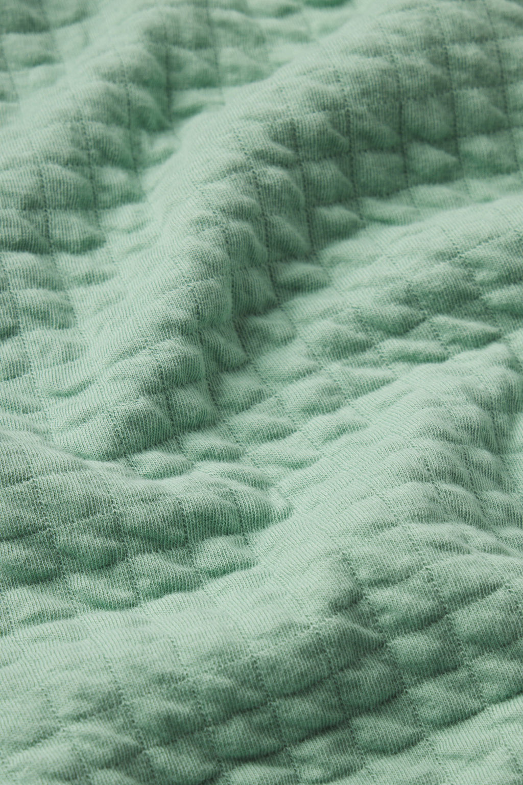 Close-up of the Jacquard Spa Robe in Granite Green shows its light green, textured, quilted fabric. Gentle folds create soft shadows and highlights, emphasizing the luxurious look and lightweight feel of this spa robe material.