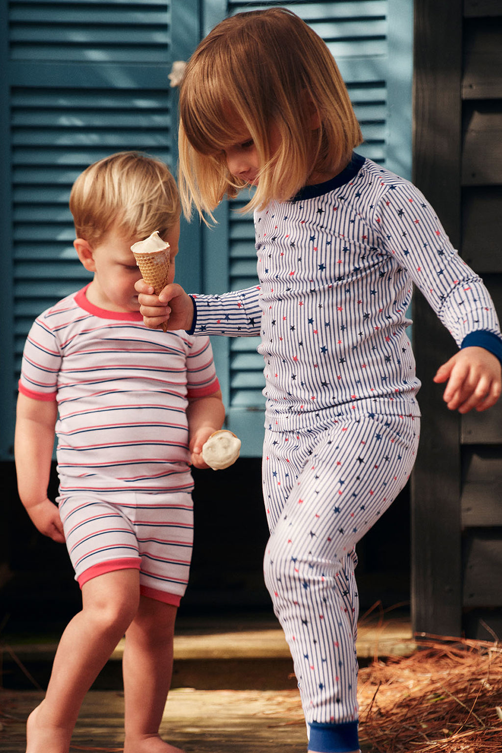 Child wearing striped pajama set with stars and red accents while holding ice cream cone next to younger child in matching st
