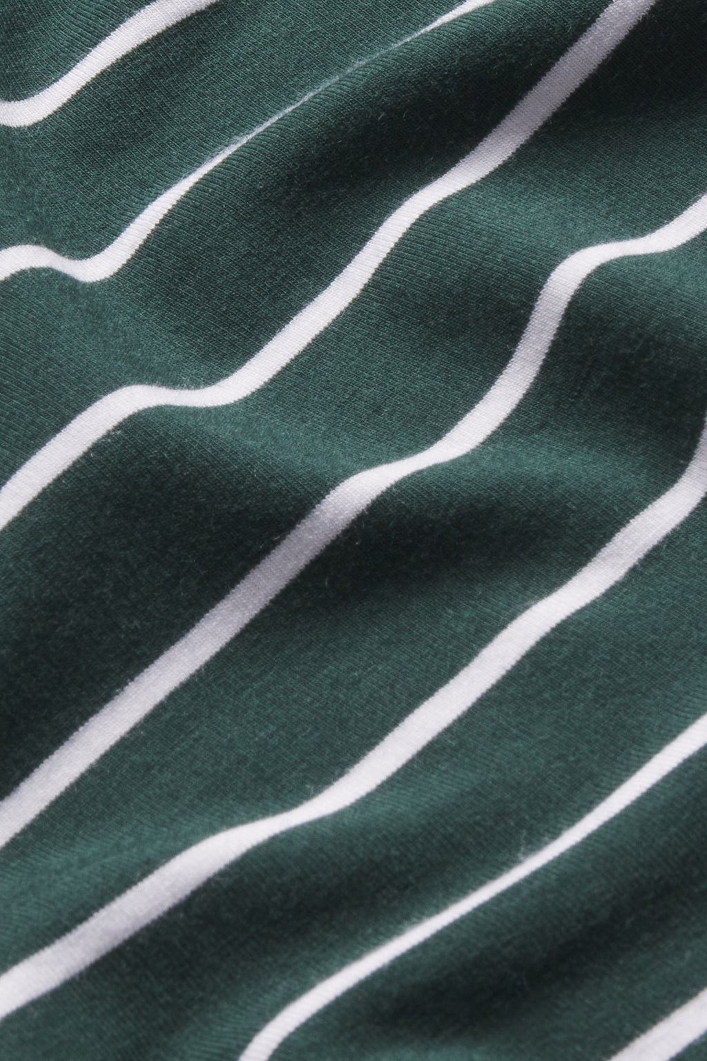 A close-up of the DreamModal Kimono Pajama Set in Conifer Stripe shows dark green modal fabric with diagonal white stripes. The slightly wrinkled material forms gentle folds and subtle shadows.