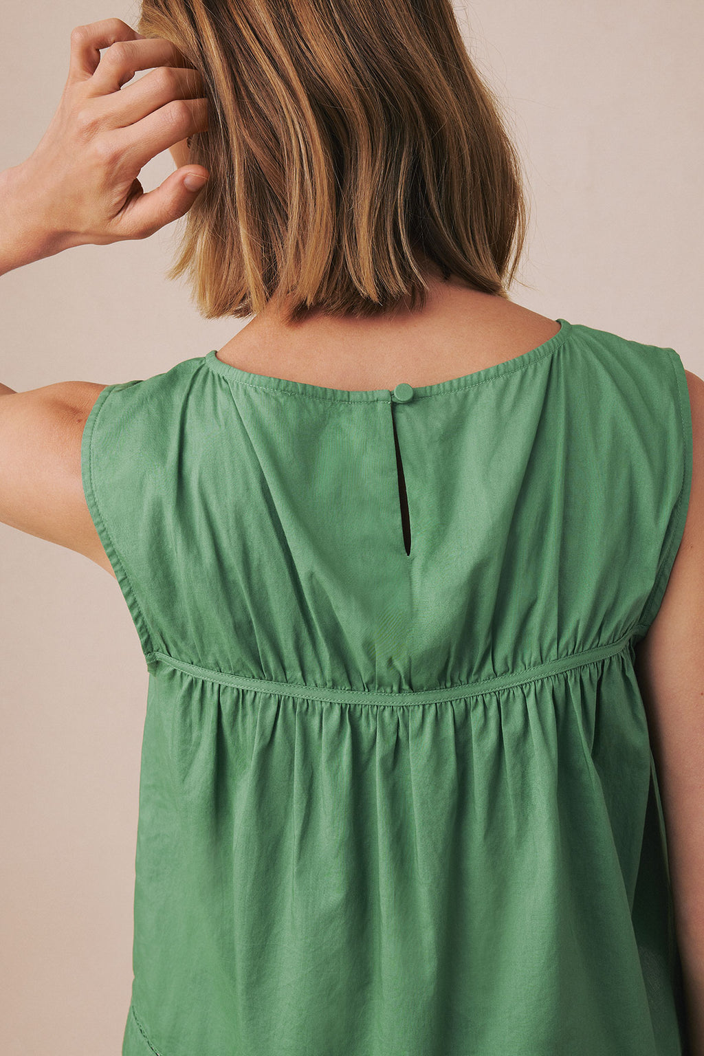 Green sleeveless tank top with gathered waist and back button closure, shown from behind on model.