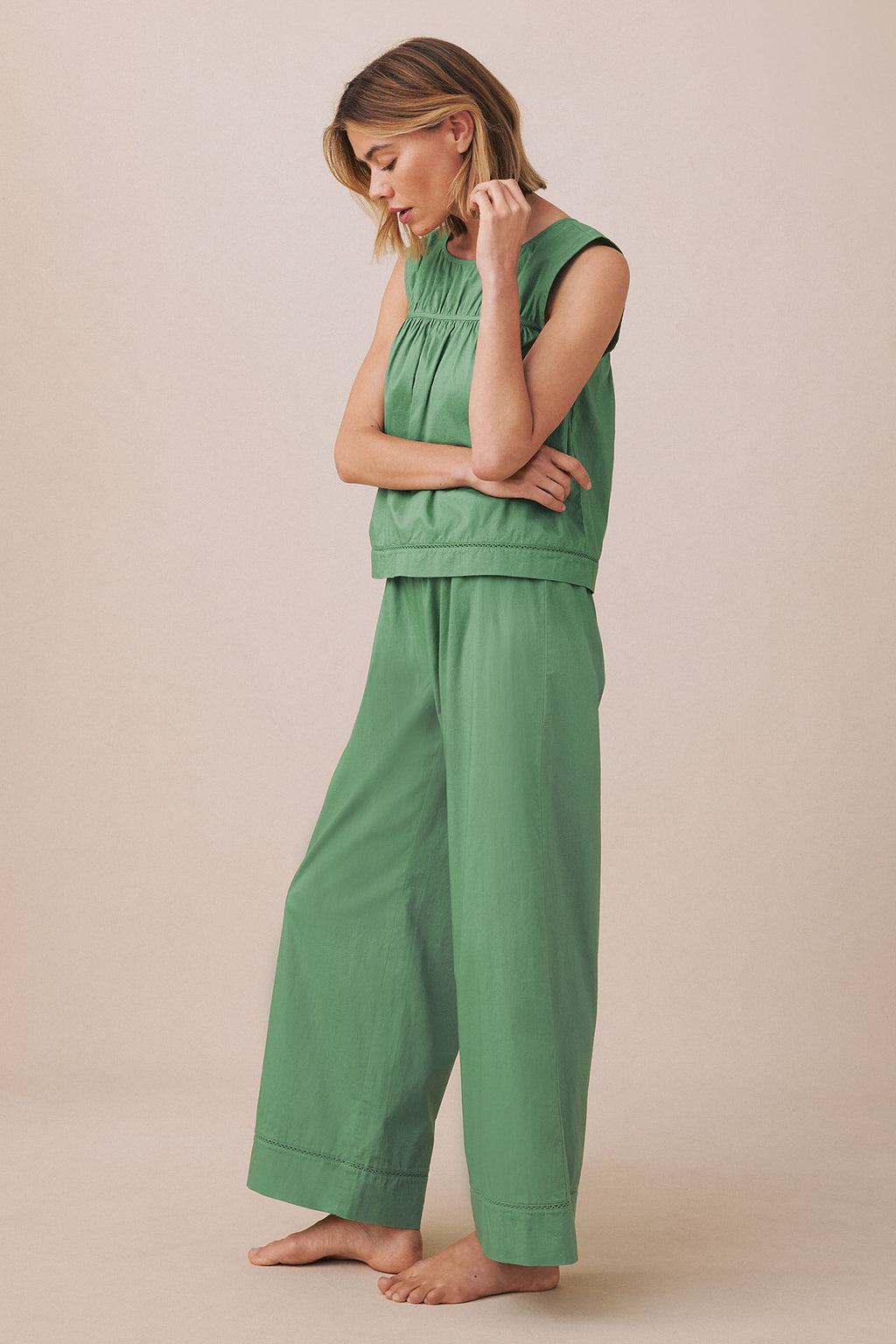Woman wearing green sleeveless tank top and matching wide-leg pants standing against beige background.