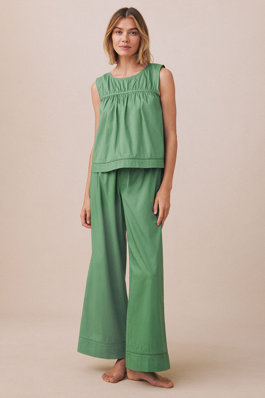 Woman wearing a green sleeveless tank top and matching long wide-leg pants with decorative stitching details.