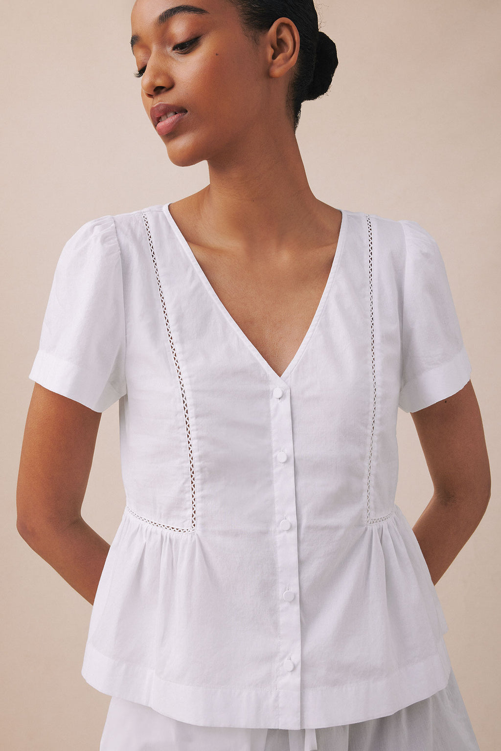 White button-front top with short sleeves, V-neckline, and decorative stitching details on the sides.