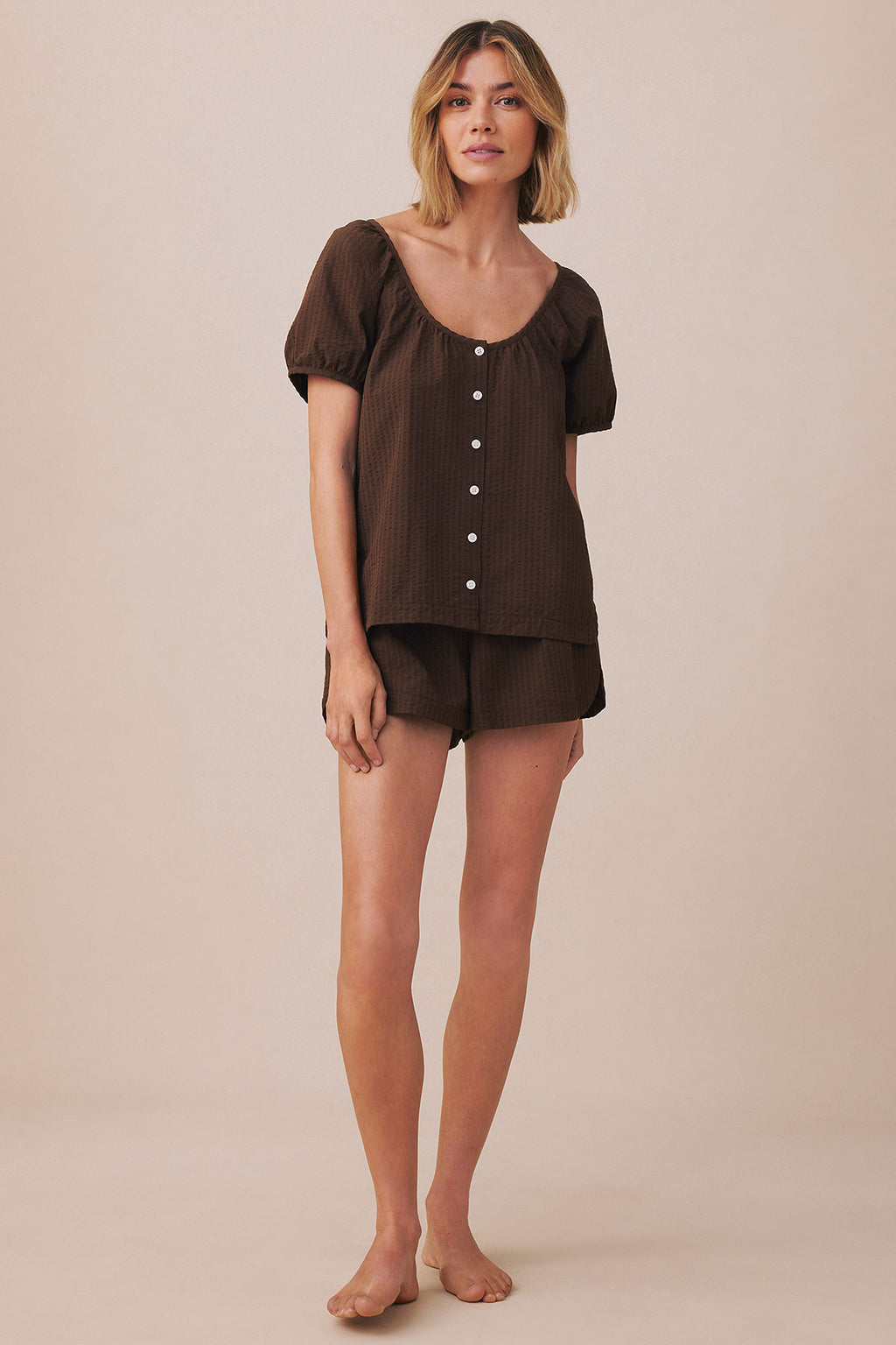 Woman wearing cocoa brown seersucker shorts set with puffed sleeves and button front top.