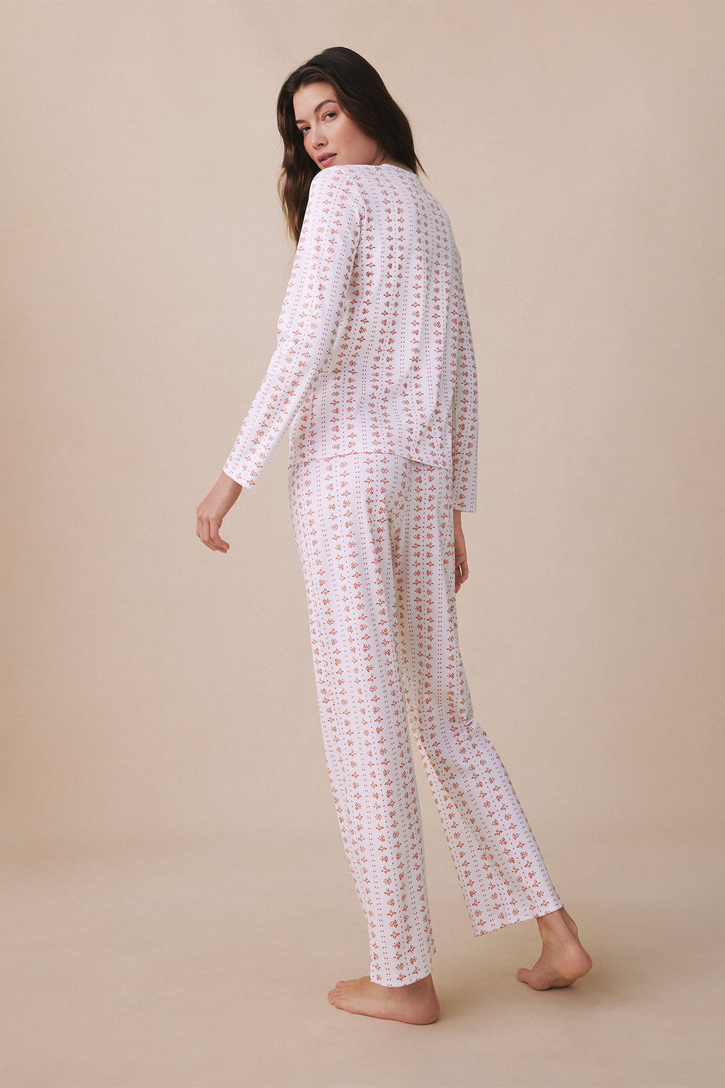Woman wearing long-sleeve crew neck pajama set with pink and tan floral print throughout.