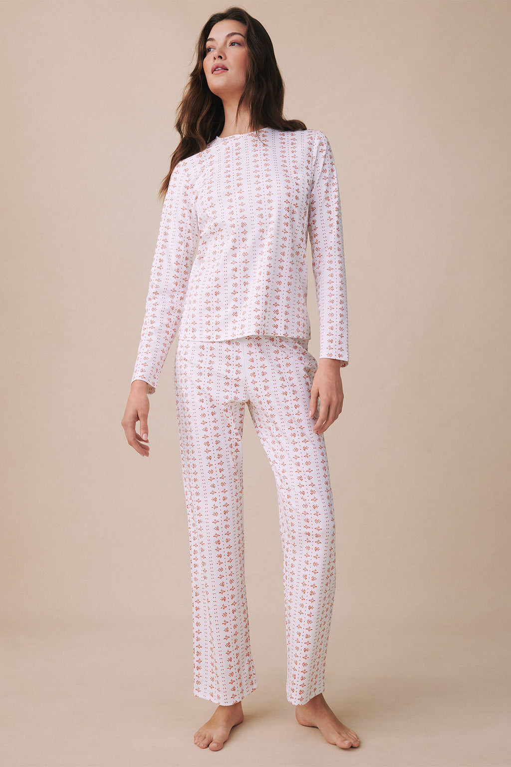 Woman wearing white long-sleeve crew neck top and matching long pants with small red floral print throughout.