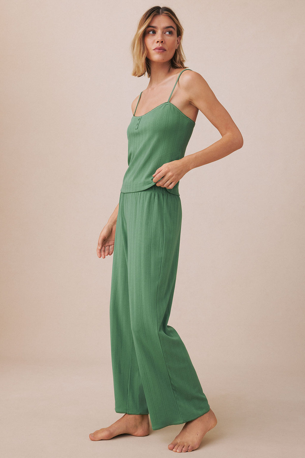 Woman wearing green ribbed camisole and wide-leg pants with thin straps against neutral background.