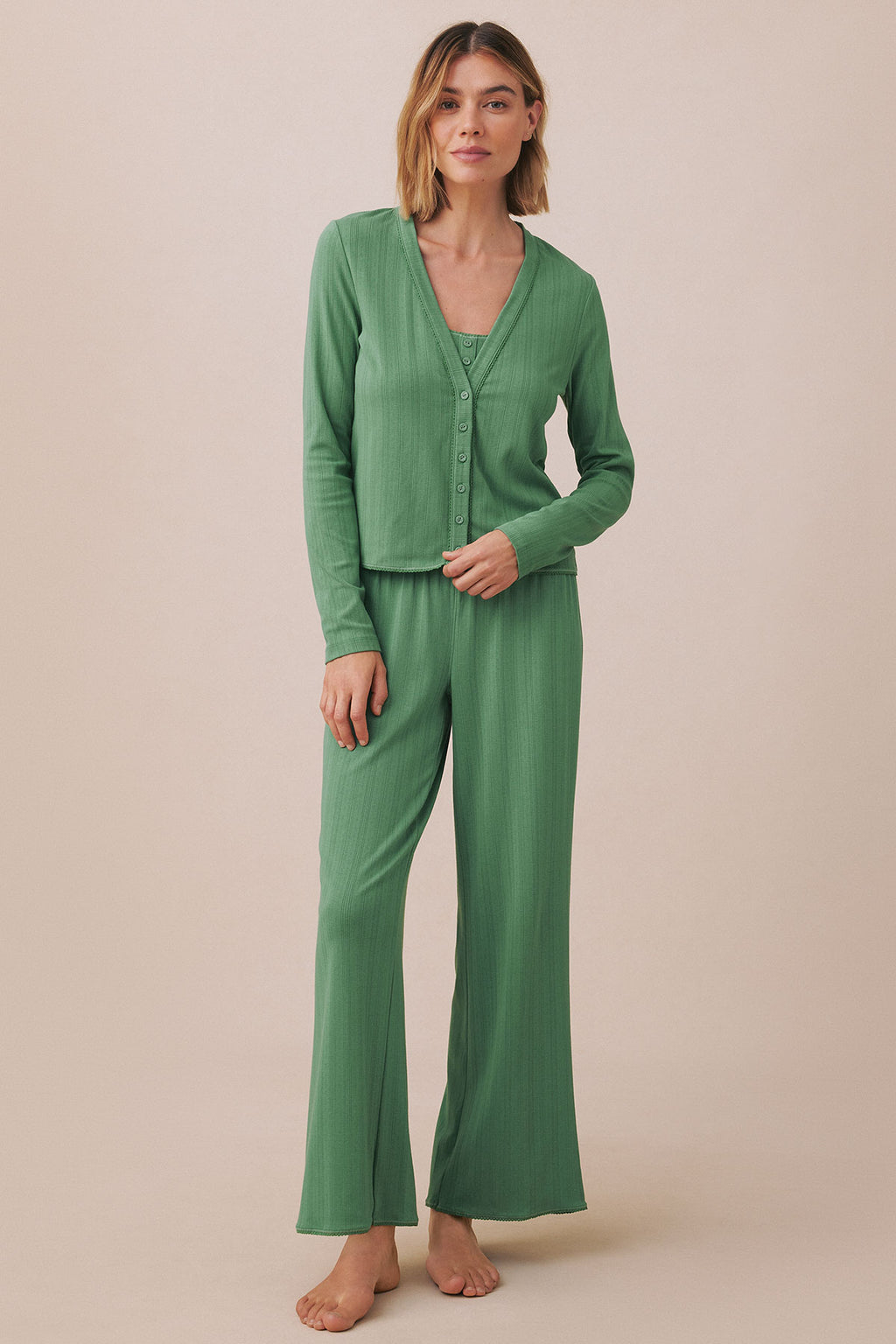 Woman wearing a green pointelle cardigan and matching pants set with button front closure and ribbed texture.
