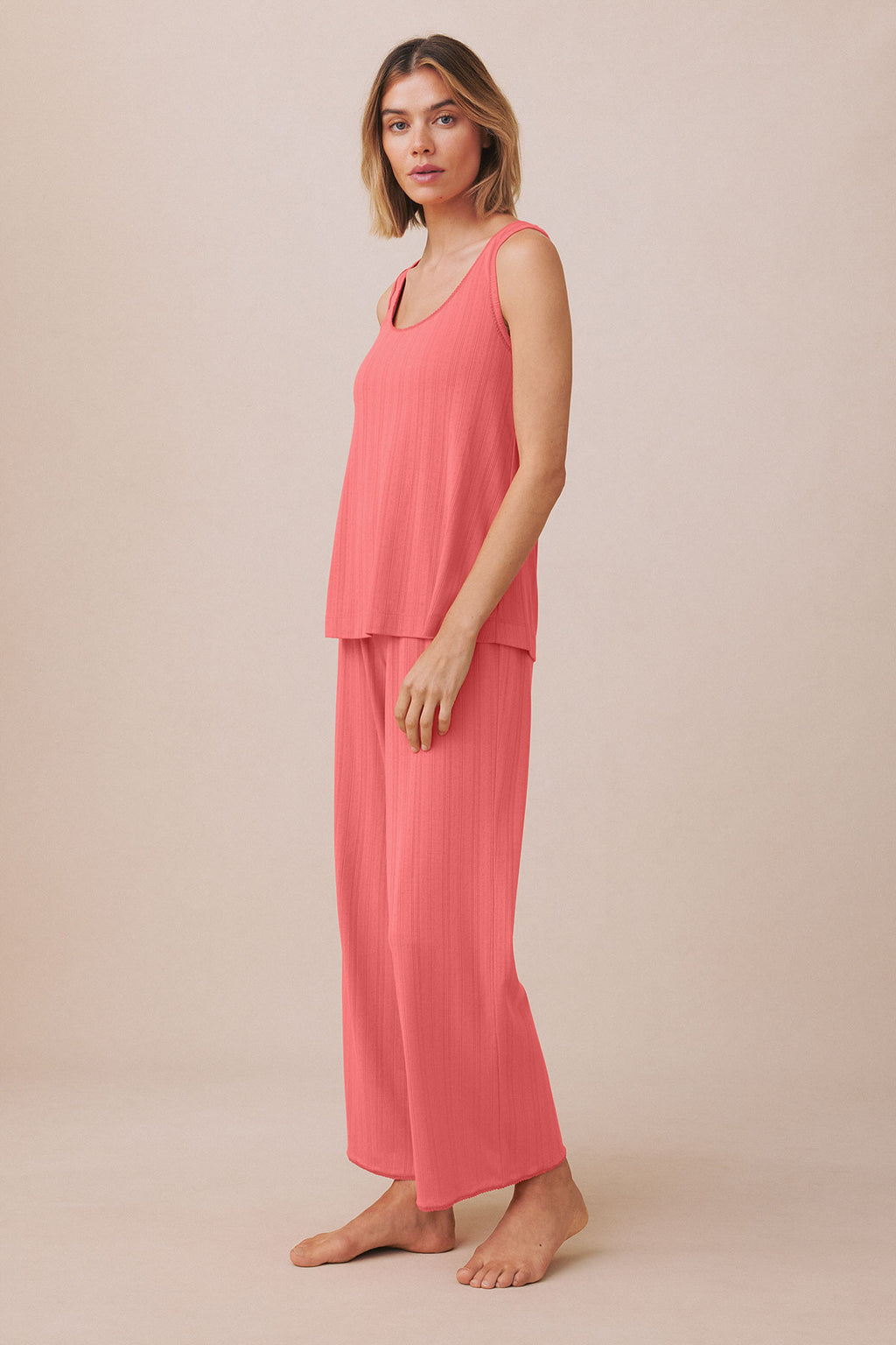 Woman wearing a coral pink ribbed sleeveless tank top and matching long pants set.