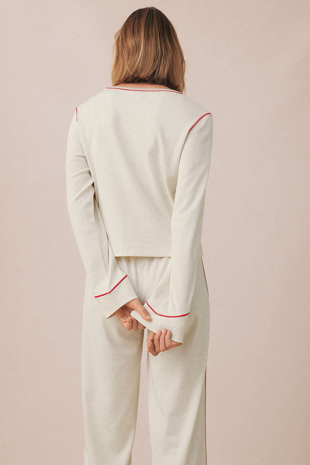 Woman wearing cream knit long-sleeve top and matching pants with red trim detail, shown from back.