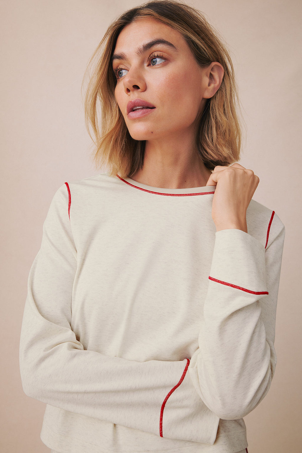 Cream long-sleeve knit top with red contrast trim on neckline, cuffs, and side seams.