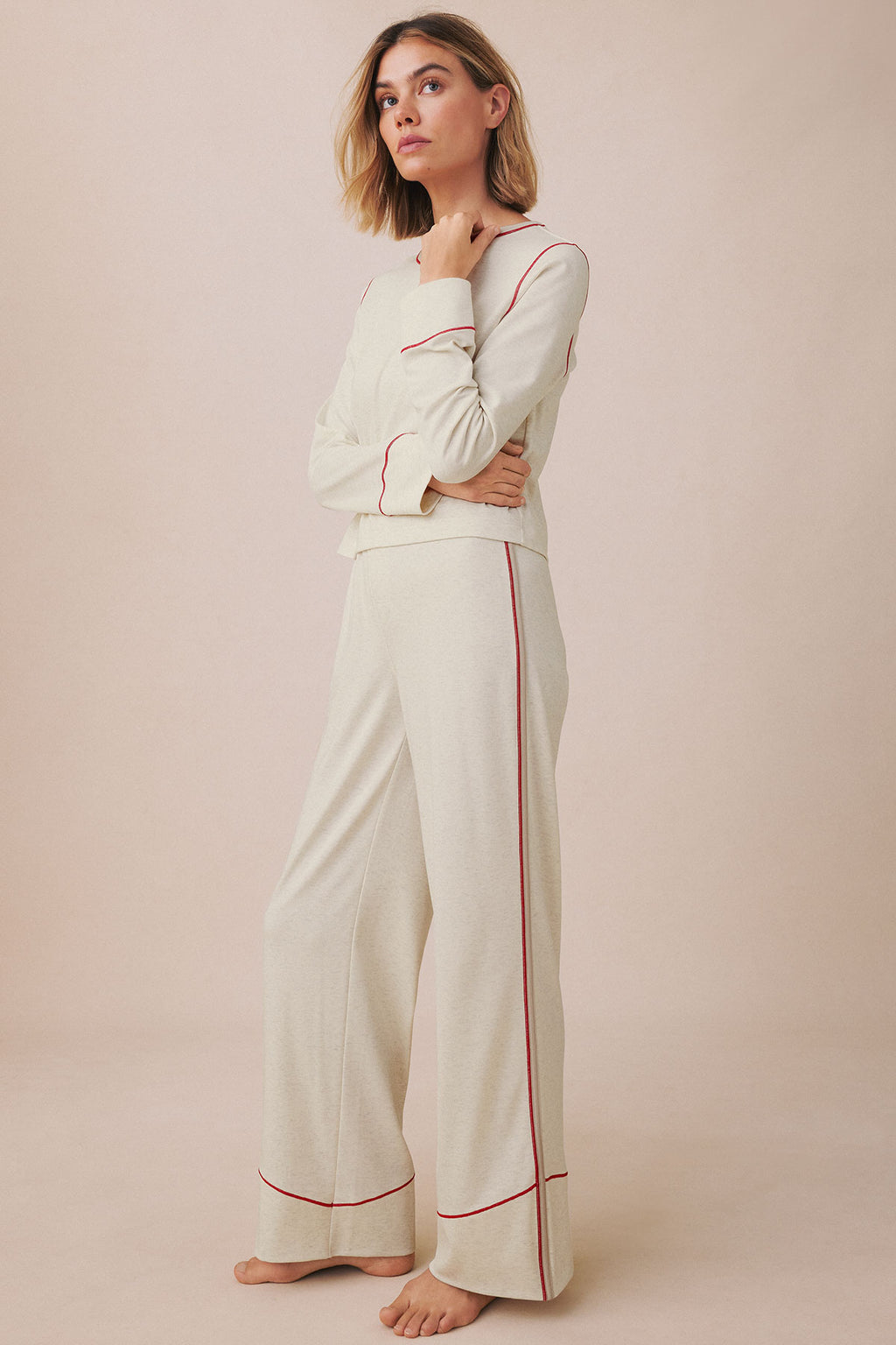 Woman wearing cream-colored knit set with long sleeves and matching wide-leg pants, featuring red trim details.