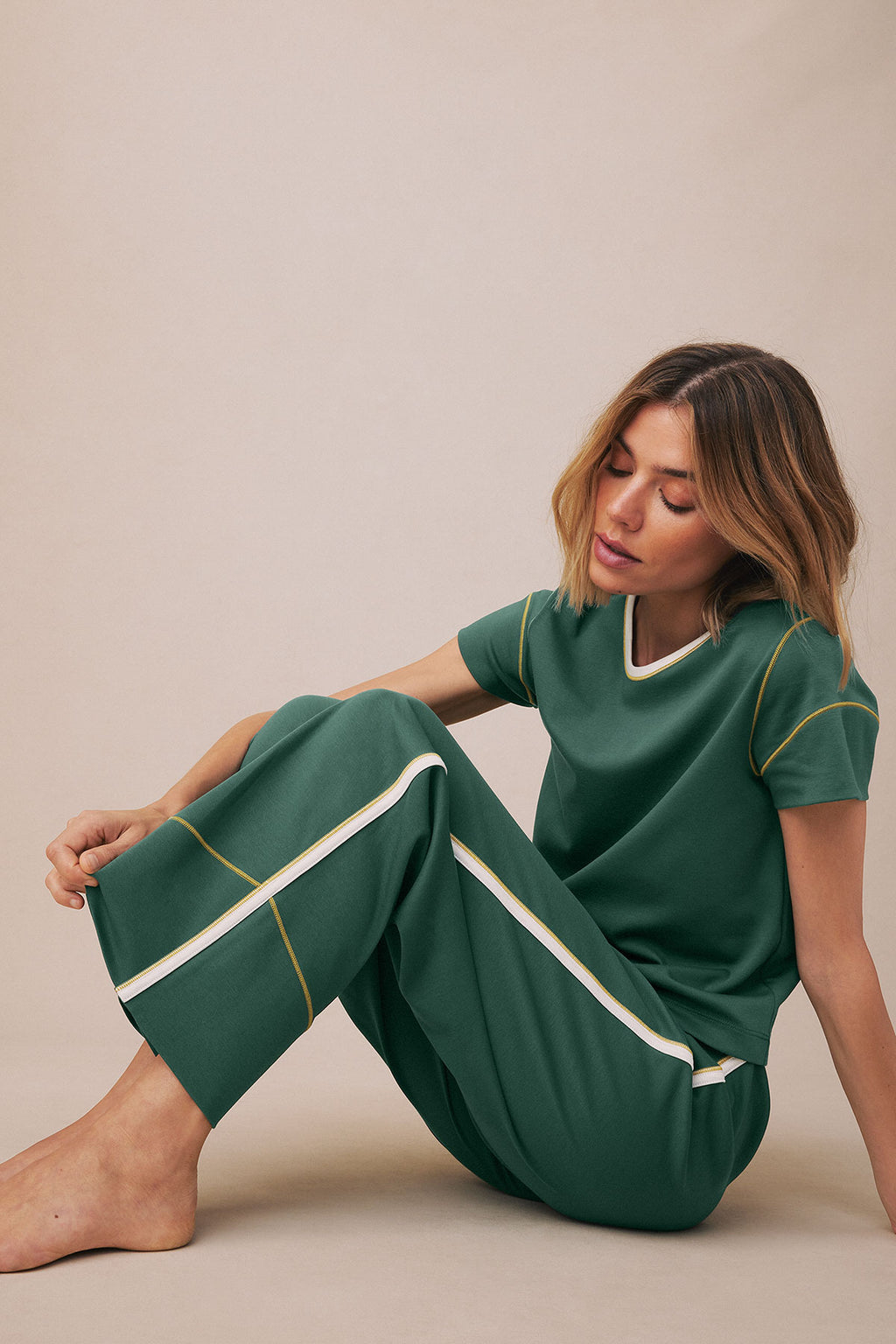 Trekking green short-sleeve top and cropped pants with white and gold trim, worn by a woman sitting against a neutral backgro