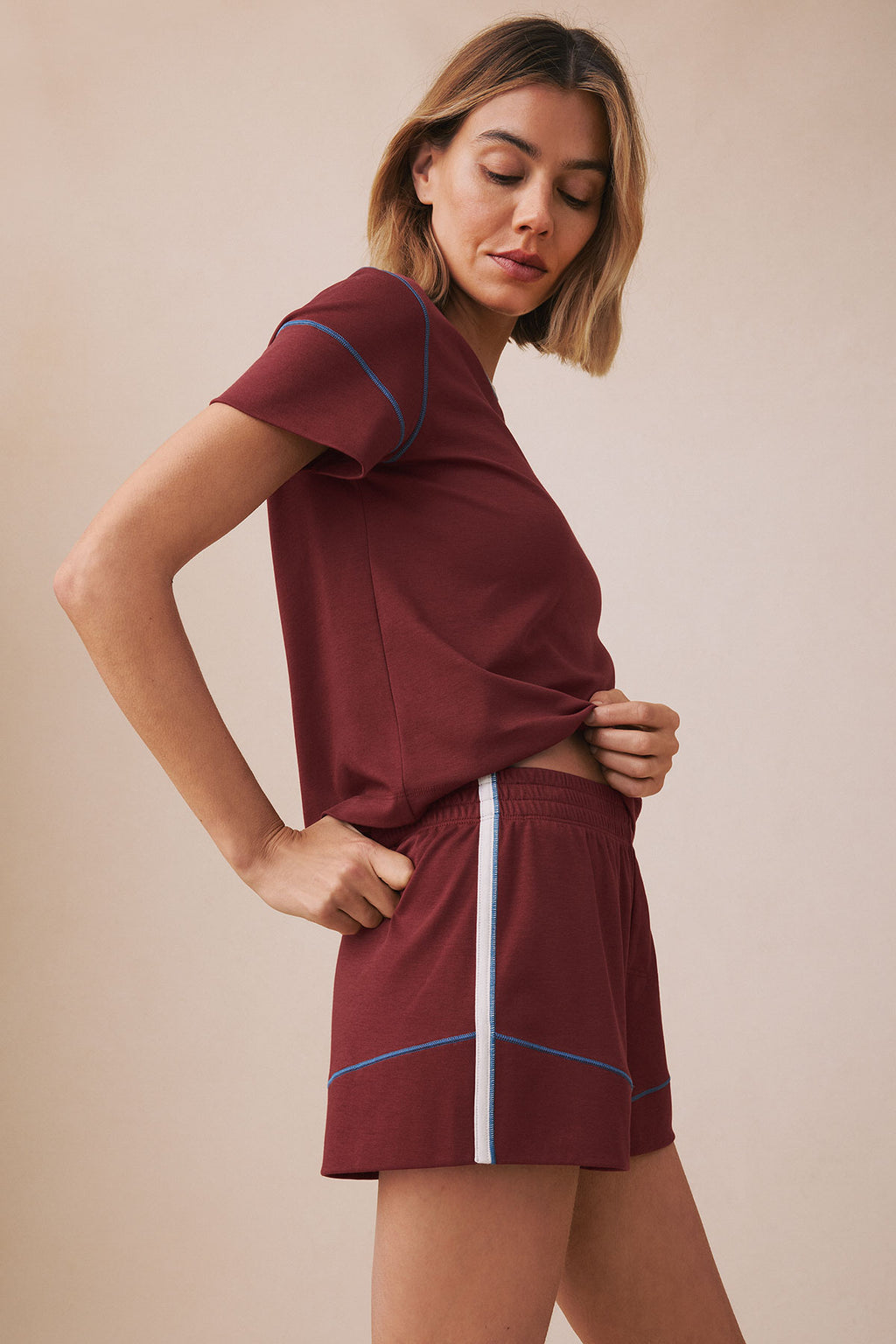 Woman wearing maroon t-shirt and matching shorts set with blue and white stripe trim details.