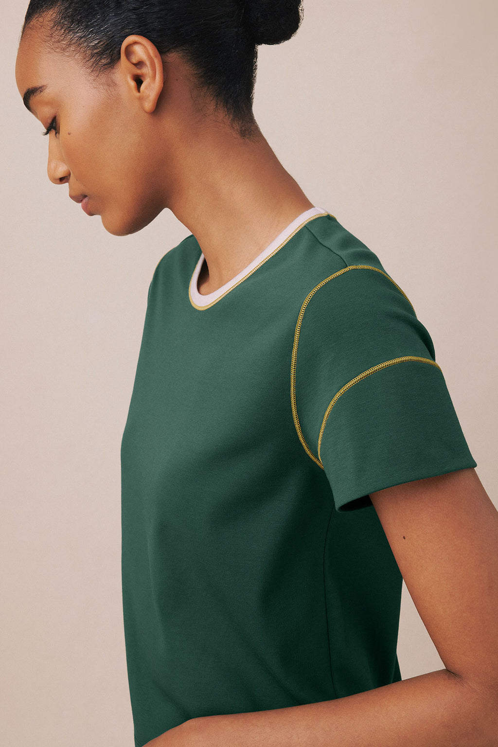Woman wearing trekking green short-sleeve top with white neckline and gold curved stitching detail on sleeve.