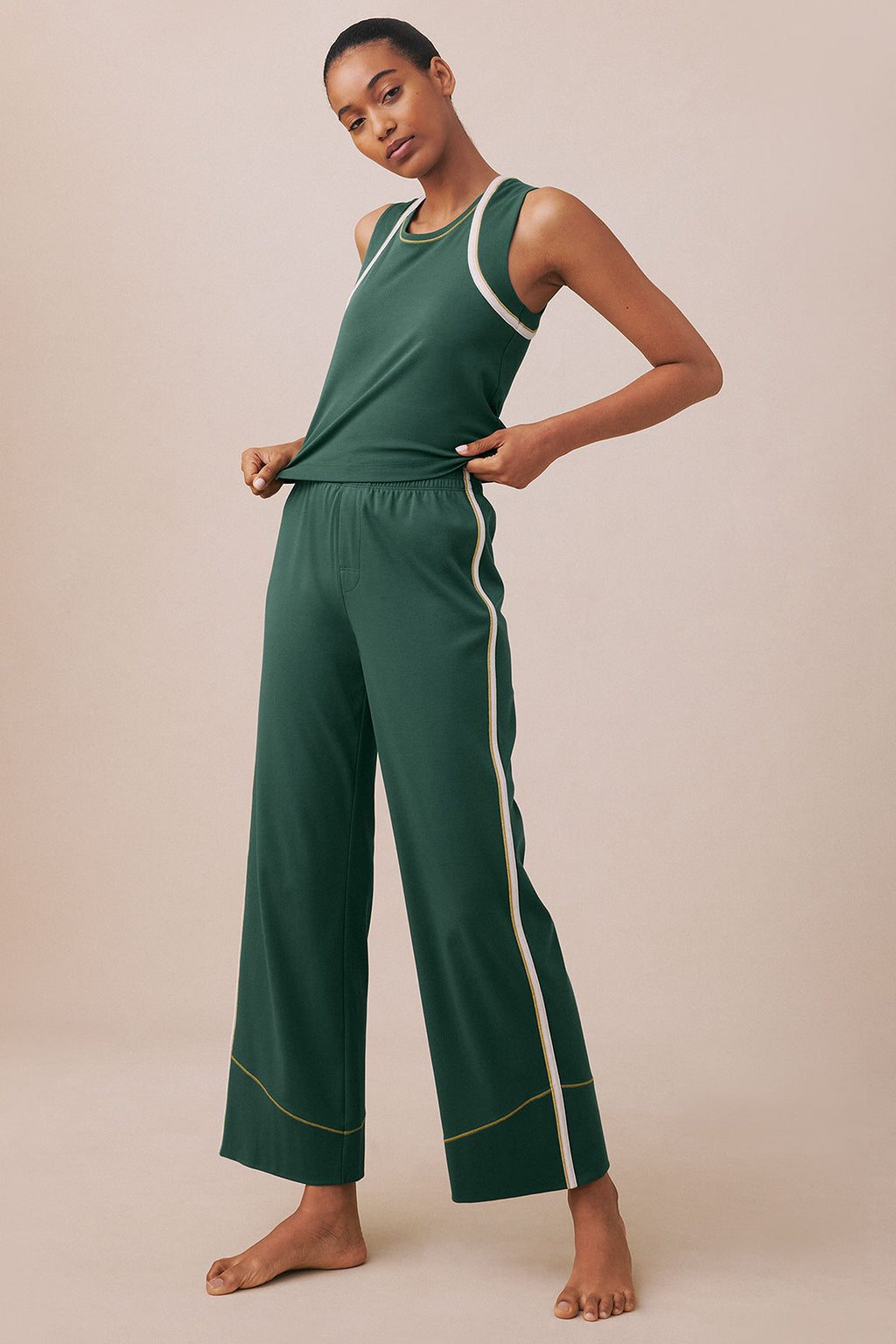 Woman wearing a trekking green sleeveless tank top and matching wide-leg pants with cream and gold trim details.