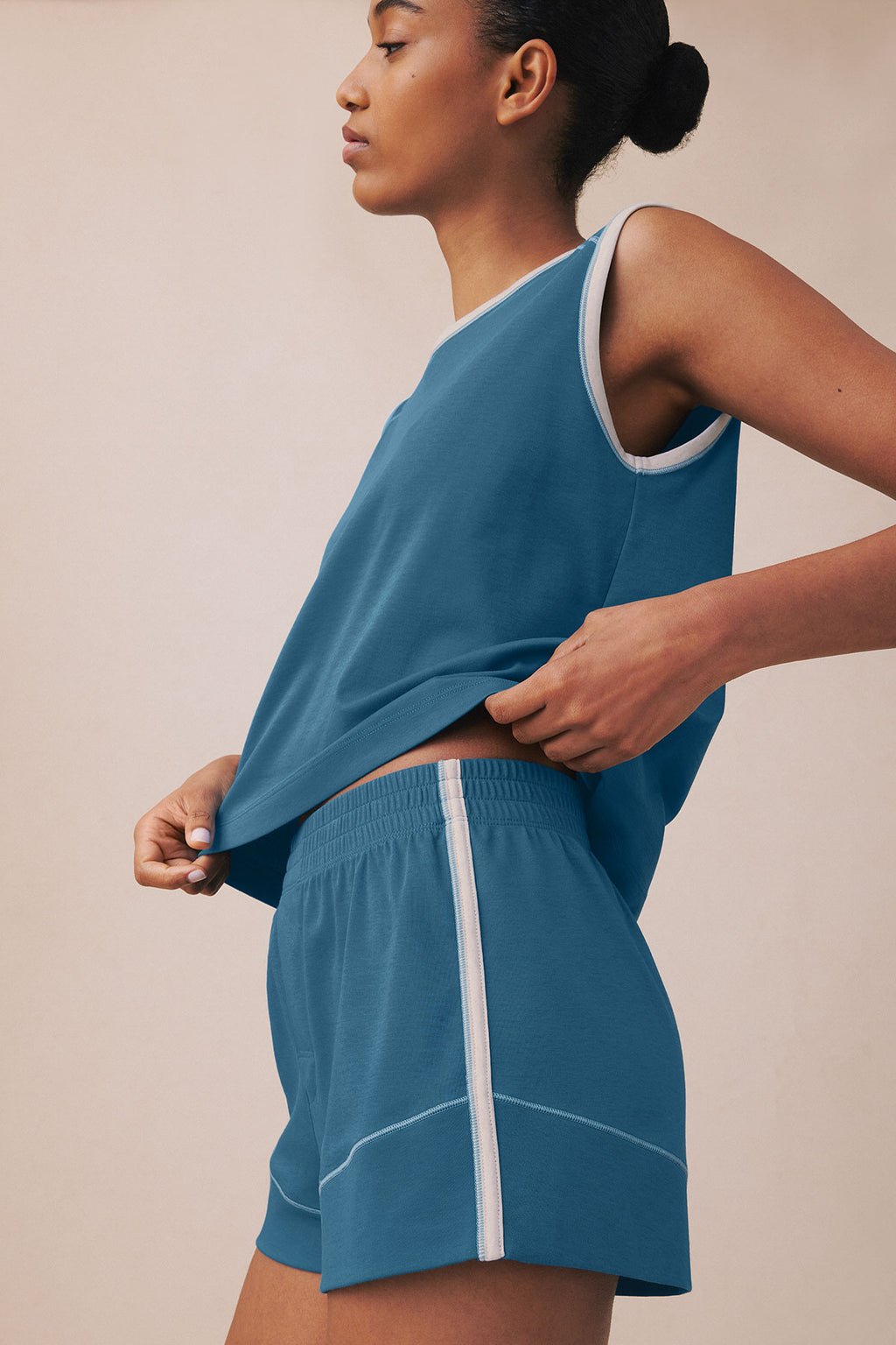 Woman wearing a blue sleeveless tank top and matching shorts with white trim and contrast stitching.