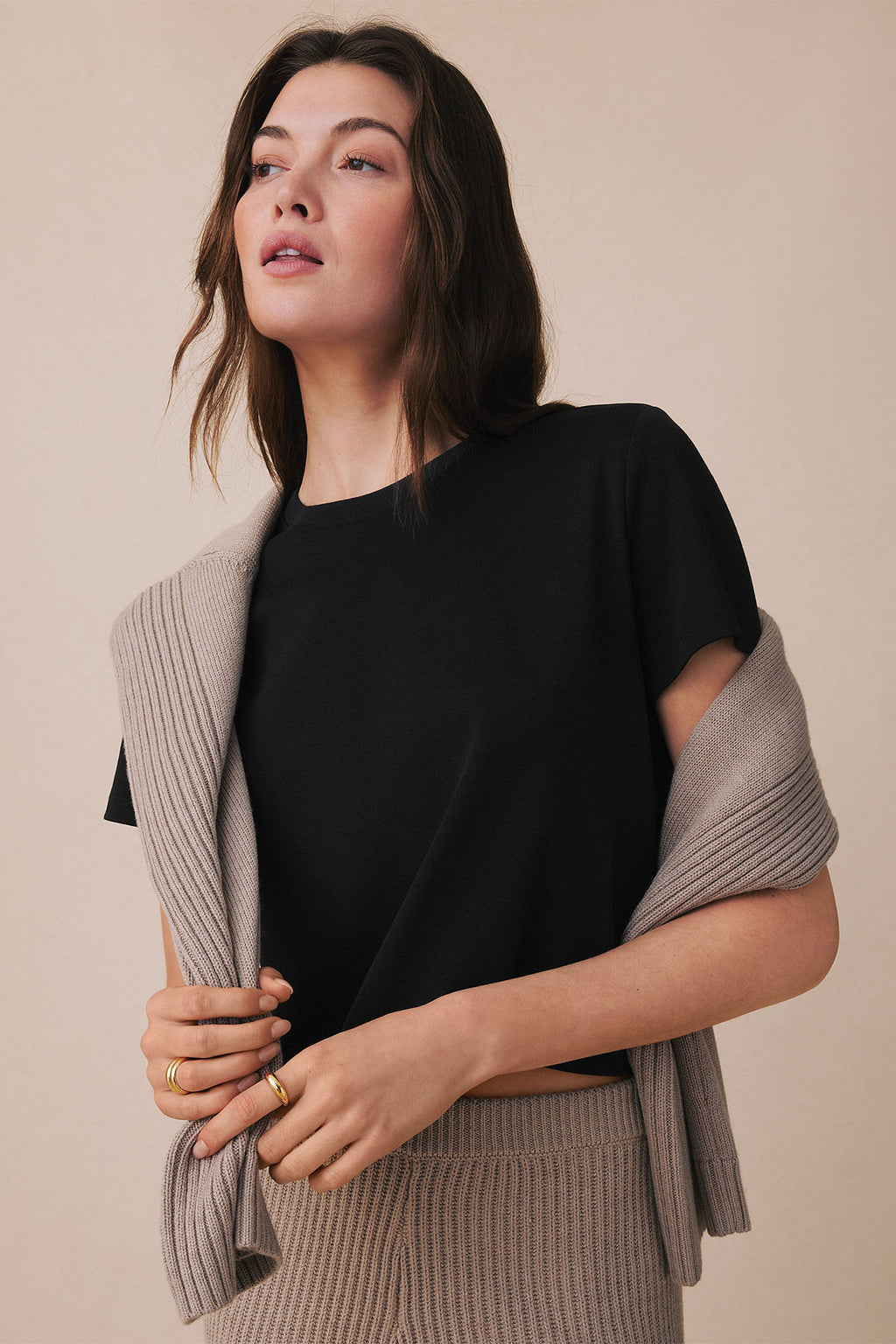 Black boxy t-shirt with crew neckline and short sleeves on model wearing beige cardigan.