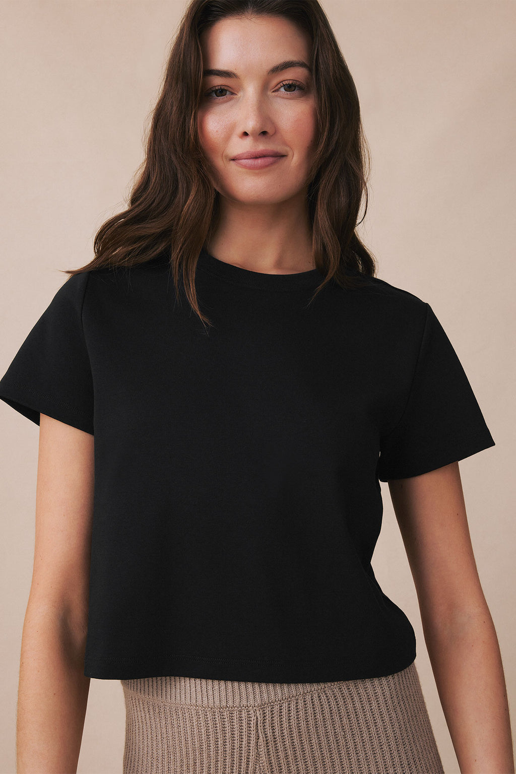 Black boxy crew neck tee with short sleeves on model wearing neutral skirt.