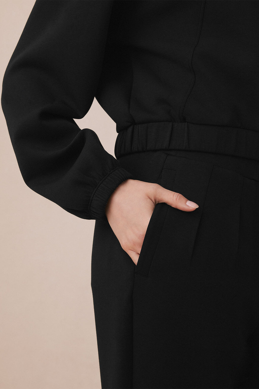 Black pants set with ribbed cuffs and side pockets, shown on model from waist to thigh.