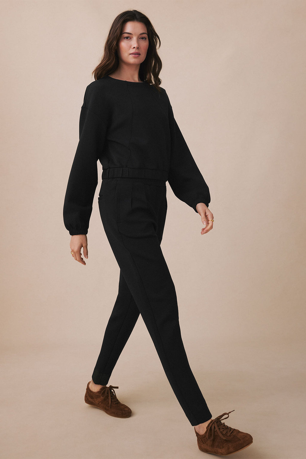 Woman wearing black long-sleeve cropped top and matching tapered pants with drawstring waist and brown suede boots.