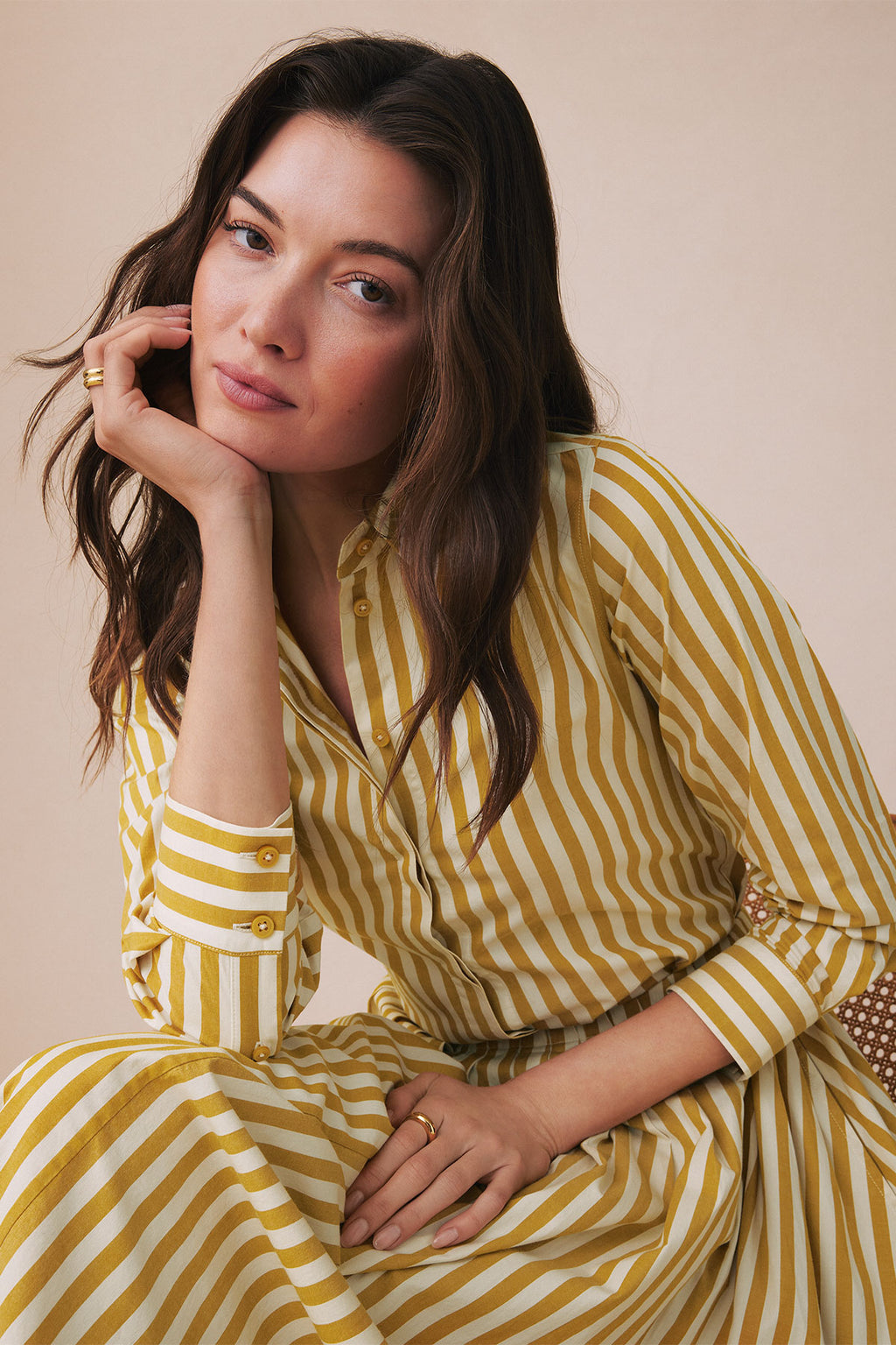 Woman wearing a gold and white striped button-up shirt and matching striped skirt with decorative cuff details.