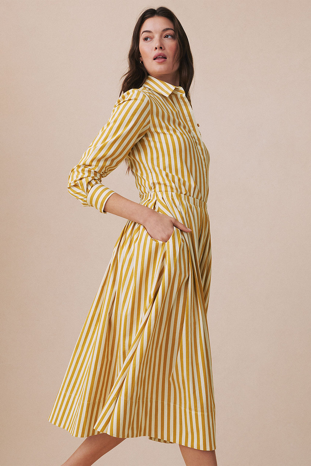 Woman wearing a gold and white vertical striped button-up shirt and matching pleated skirt set.