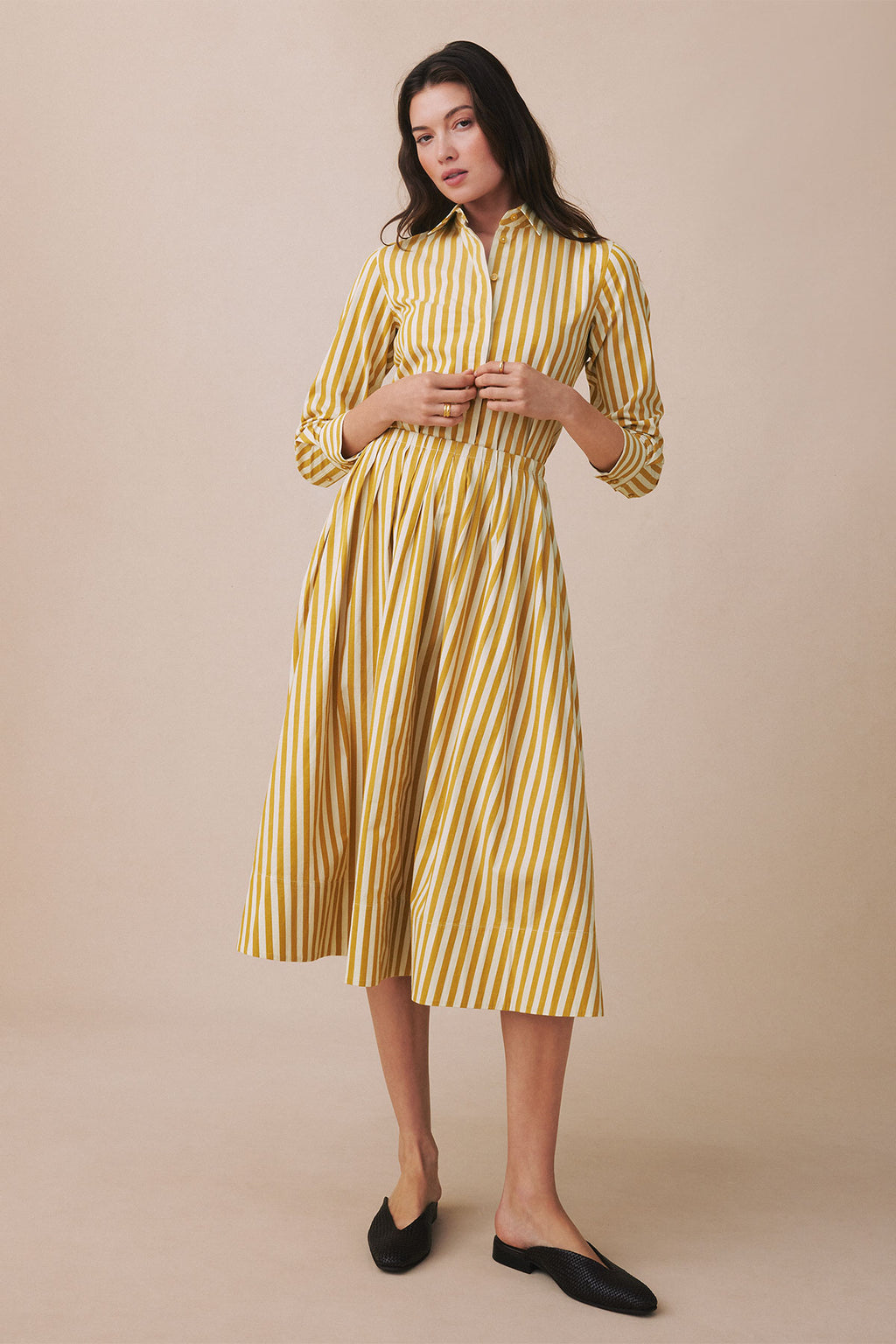 Woman wearing a yellow and white striped button-up shirt dress with three-quarter sleeves and a pleated skirt, paired with bl
