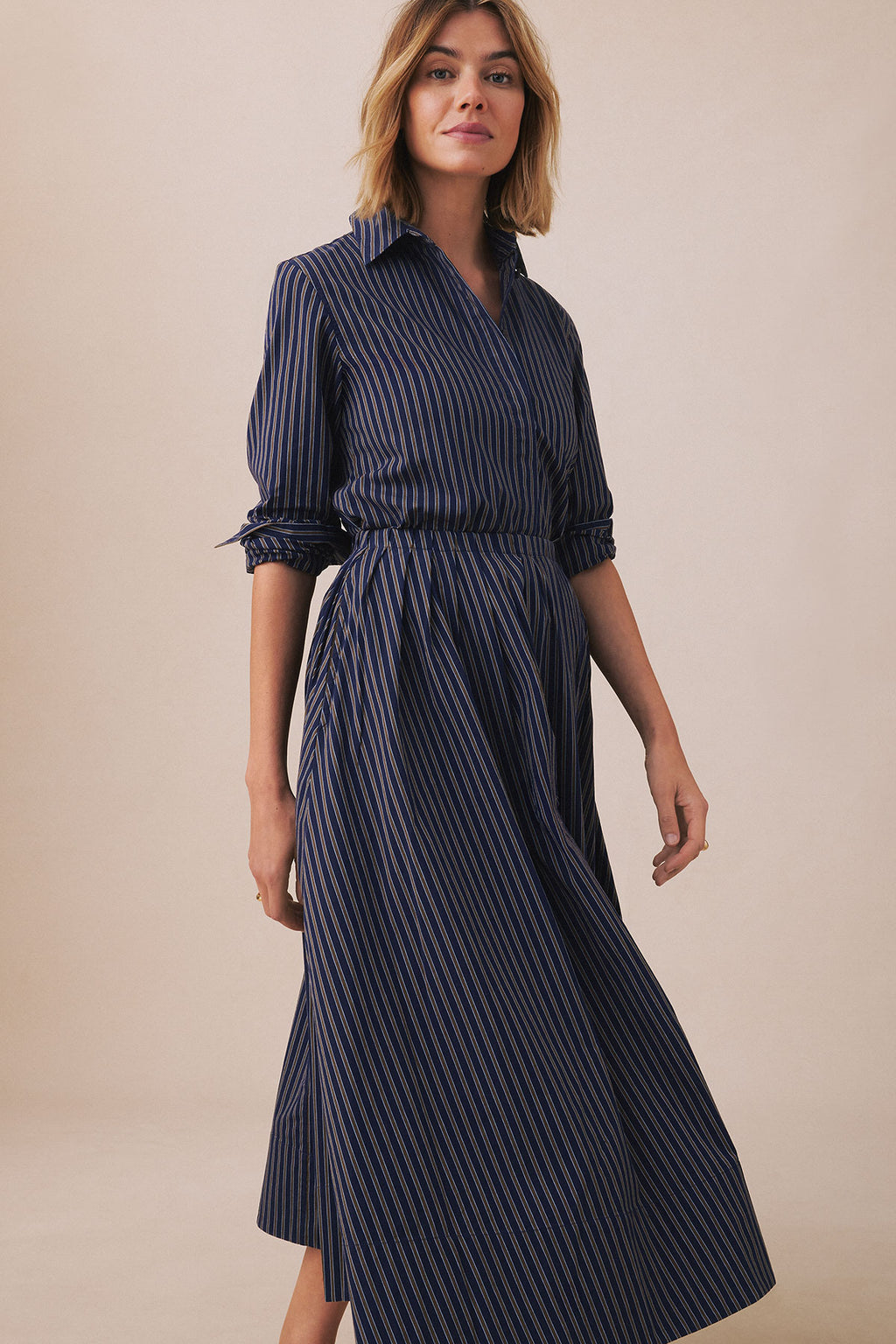 Woman wearing navy striped shirt and matching pleated skirt with three-quarter sleeves and defined waistline.