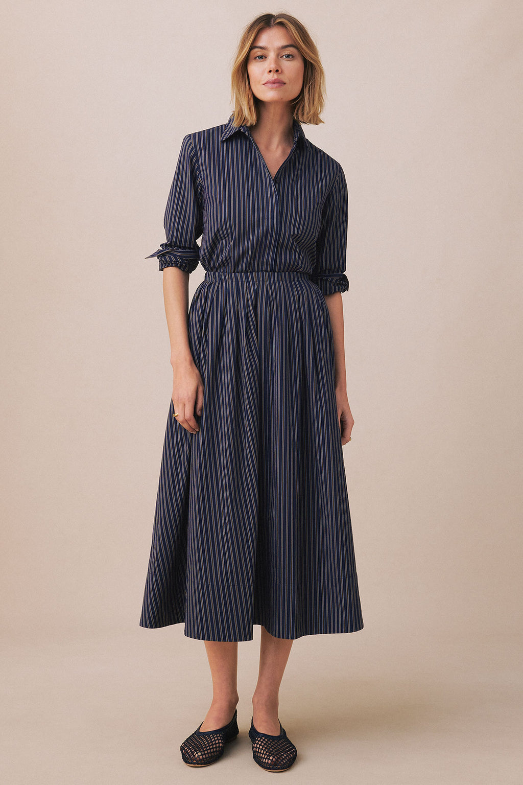Woman wearing navy striped button-up shirt and matching mid-length skirt with gathered waist and three-quarter sleeves.