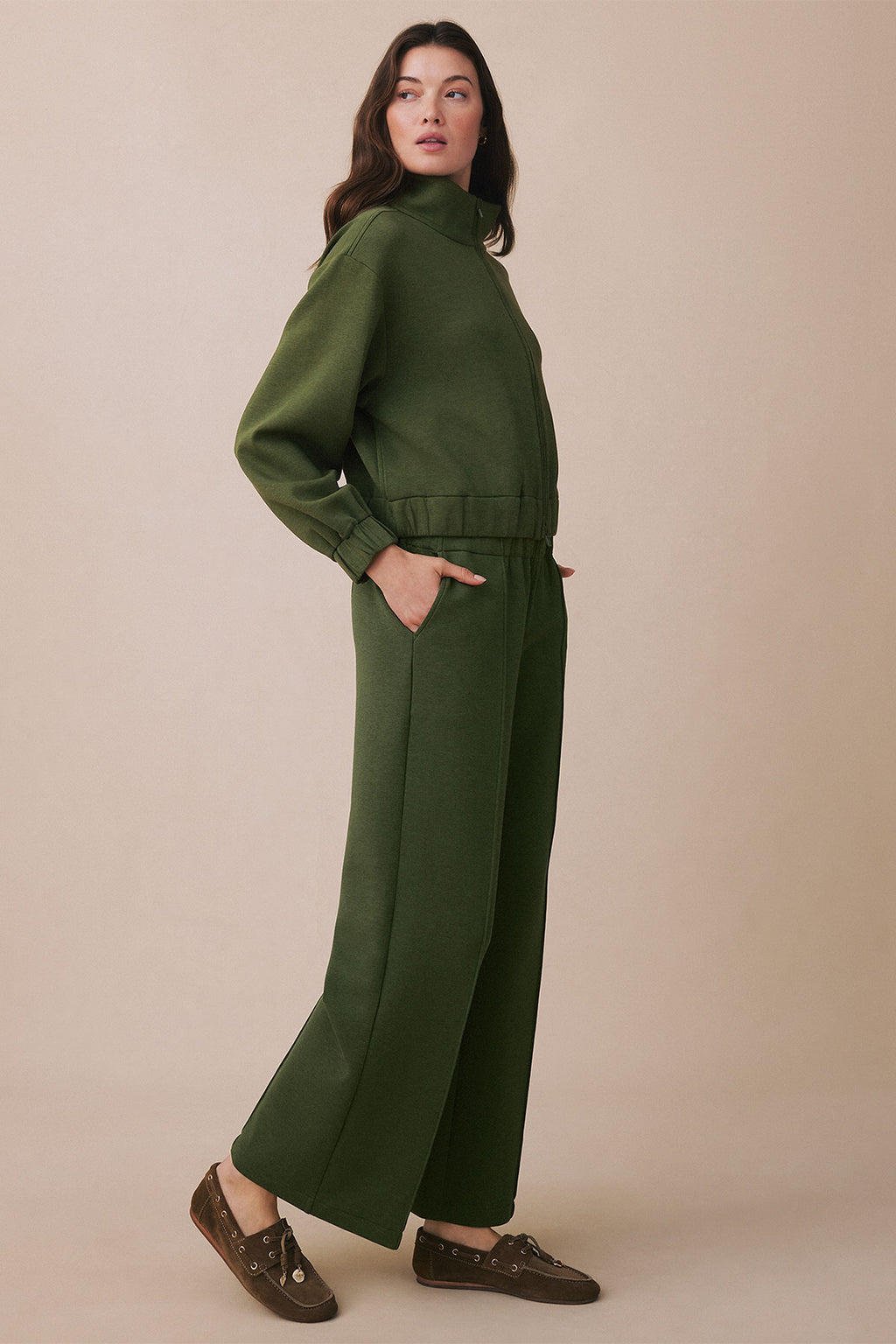 Woman wearing cedar green jumpsuit with long sleeves, collared neckline, cinched waist, and wide-leg pants.