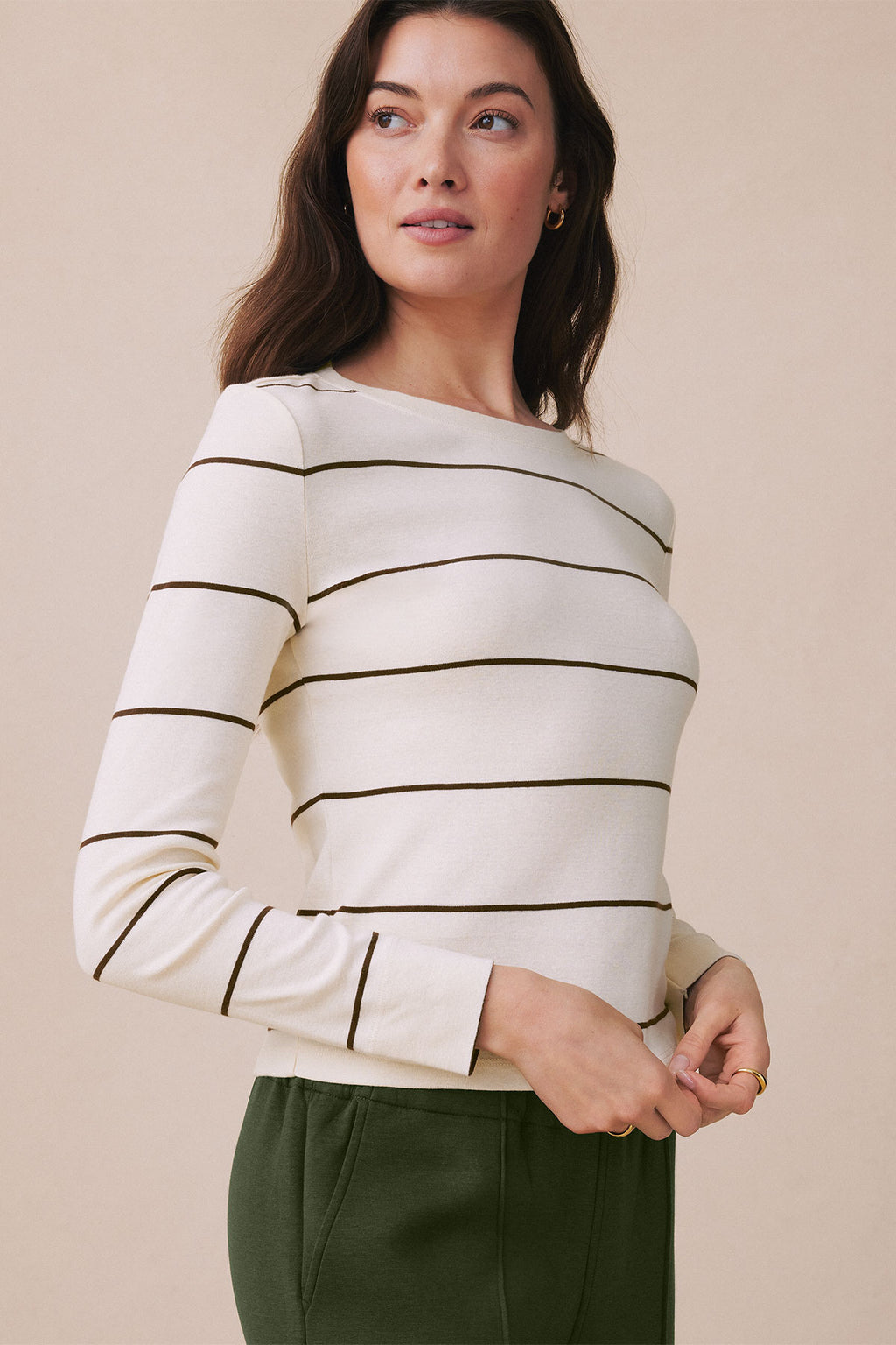 Woman wearing a cream long-sleeve striped tee with cocoa horizontal stripes and green pants.