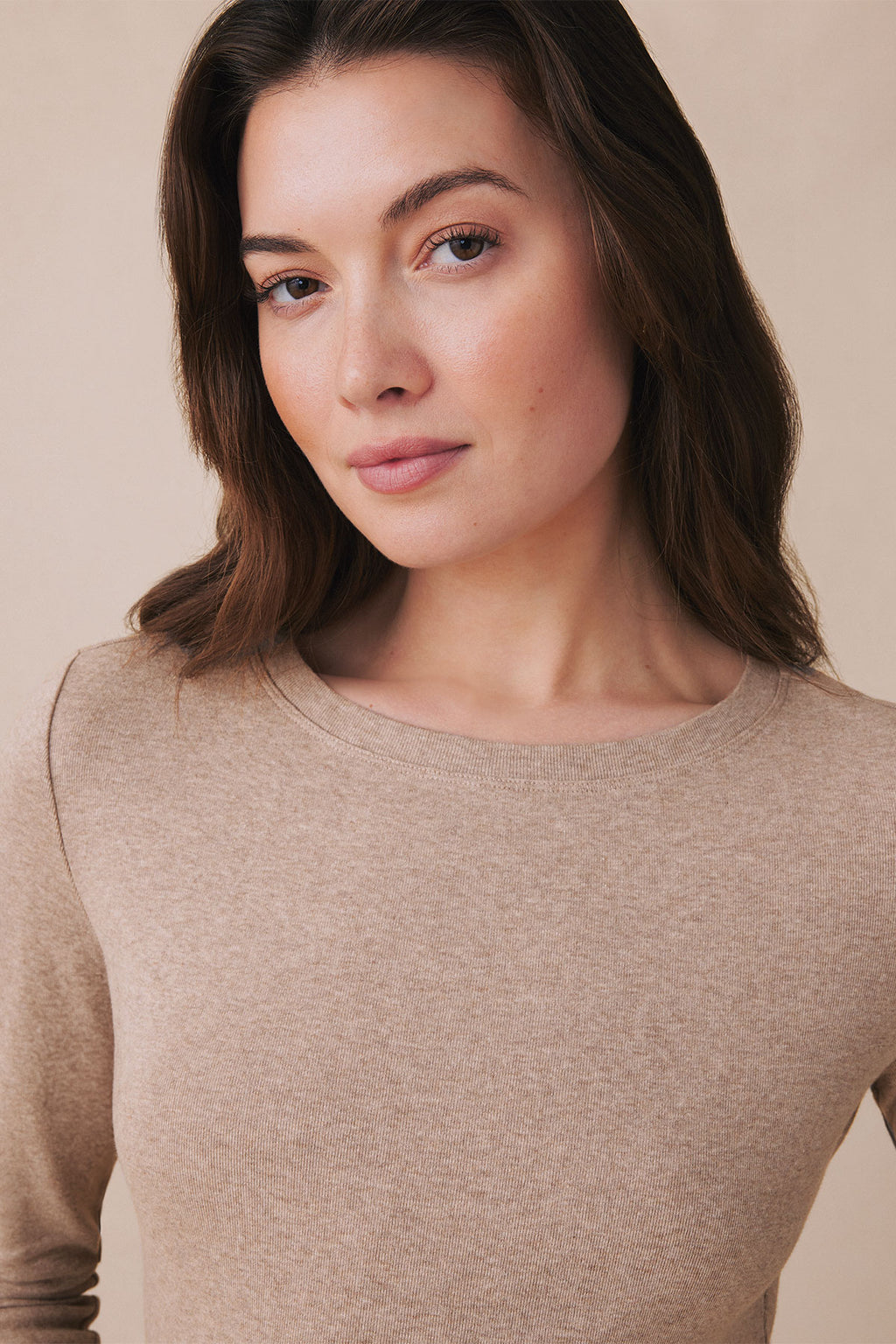 Woman wearing a fawn heather long sleeve crew neck tee against a neutral background.