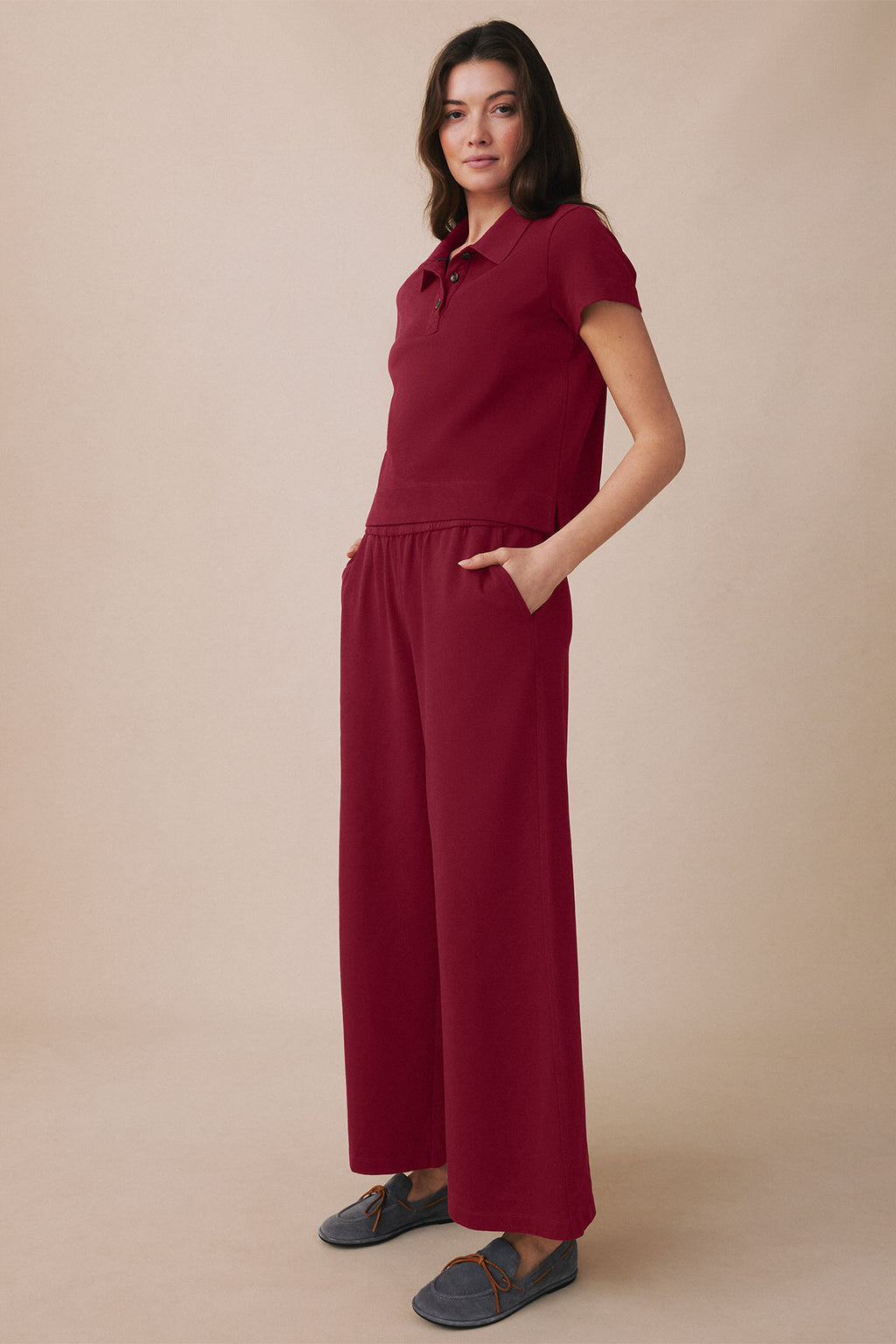 Woman wearing deep burgundy polo shirt and wide-leg pants with side pockets, styled with gray slip-on shoes.