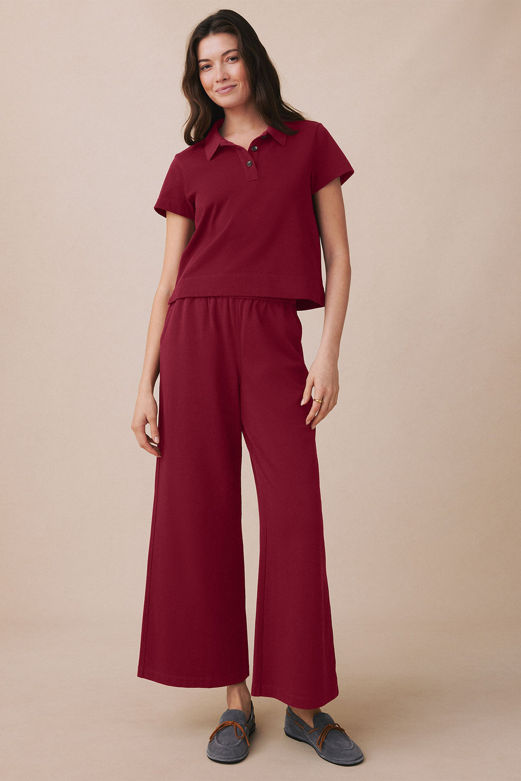Woman wearing burgundy polo shirt and matching wide-leg pants with gray loafers.