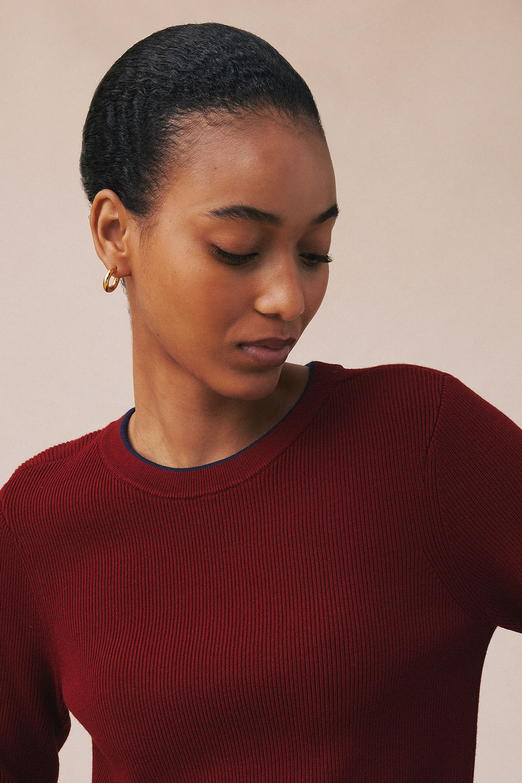 Dark red ribbed crew-neck sweater with navy trim on model against neutral background.