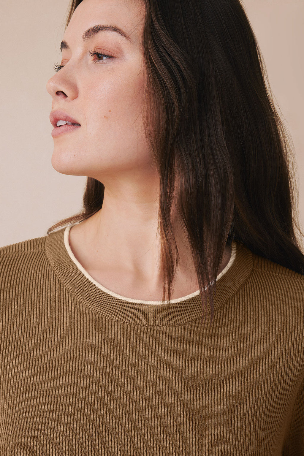 Woman wearing toffee-colored ribbed knit top with cream trim neckline, shown from side profile.